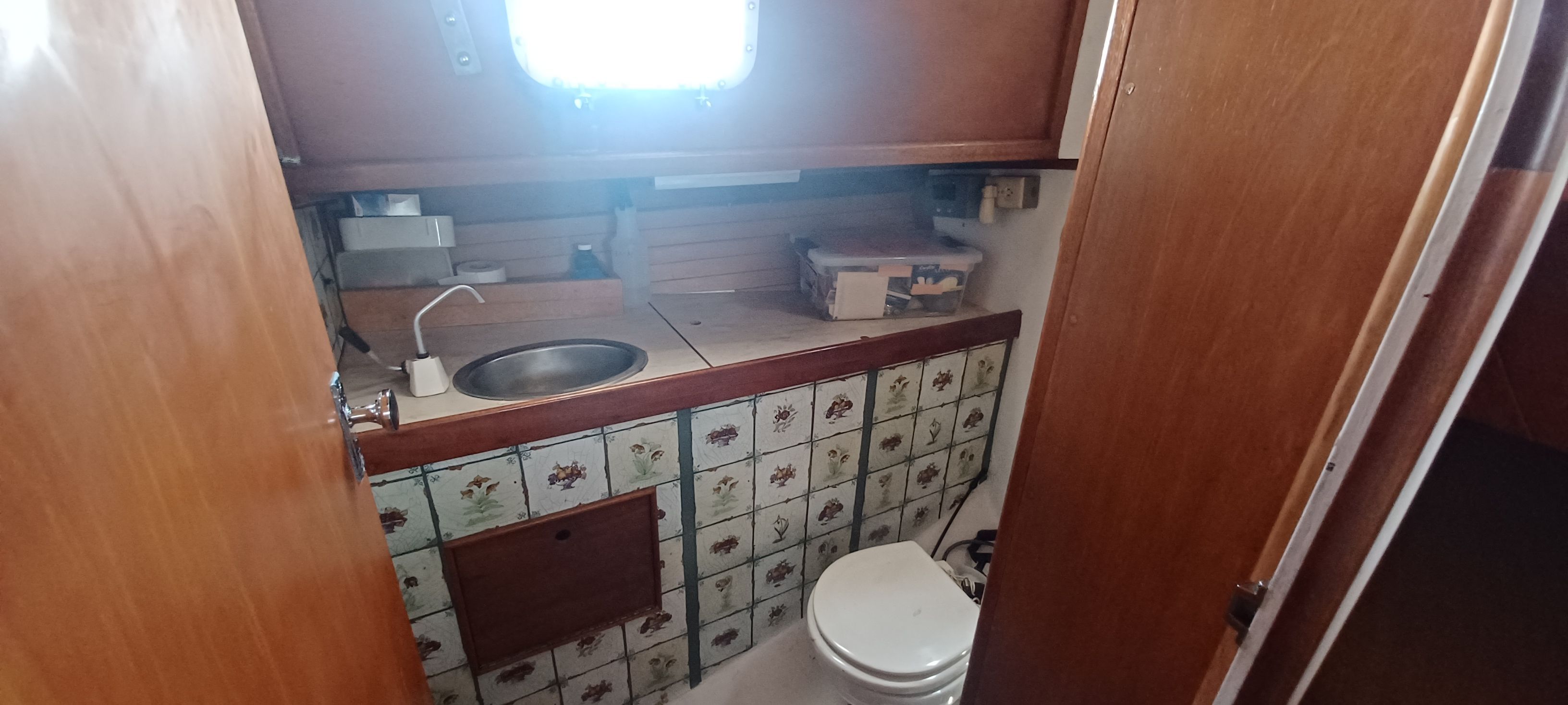 Interior of a yacht with a sink and toilet, wooden walls, and decorative tiles.
