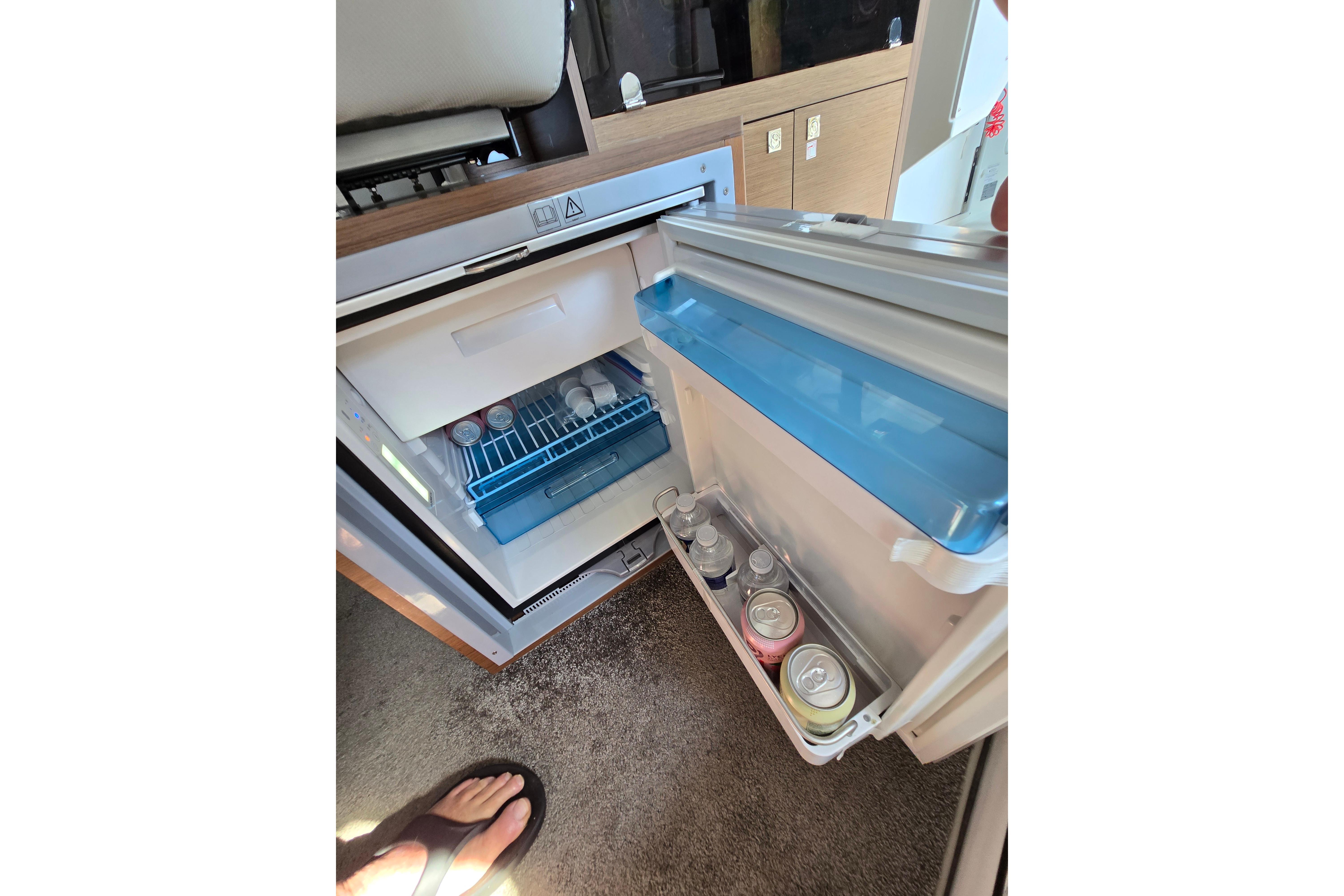 An open fridge on a boat with beverage cans inside.