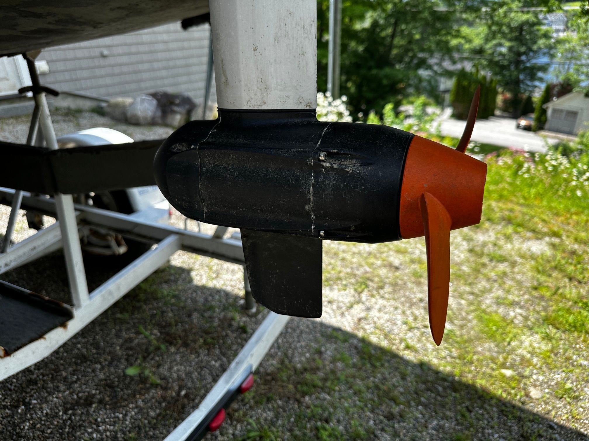 Close-up of a propeller on a boat on a trailer, surrounded by grass and trees.