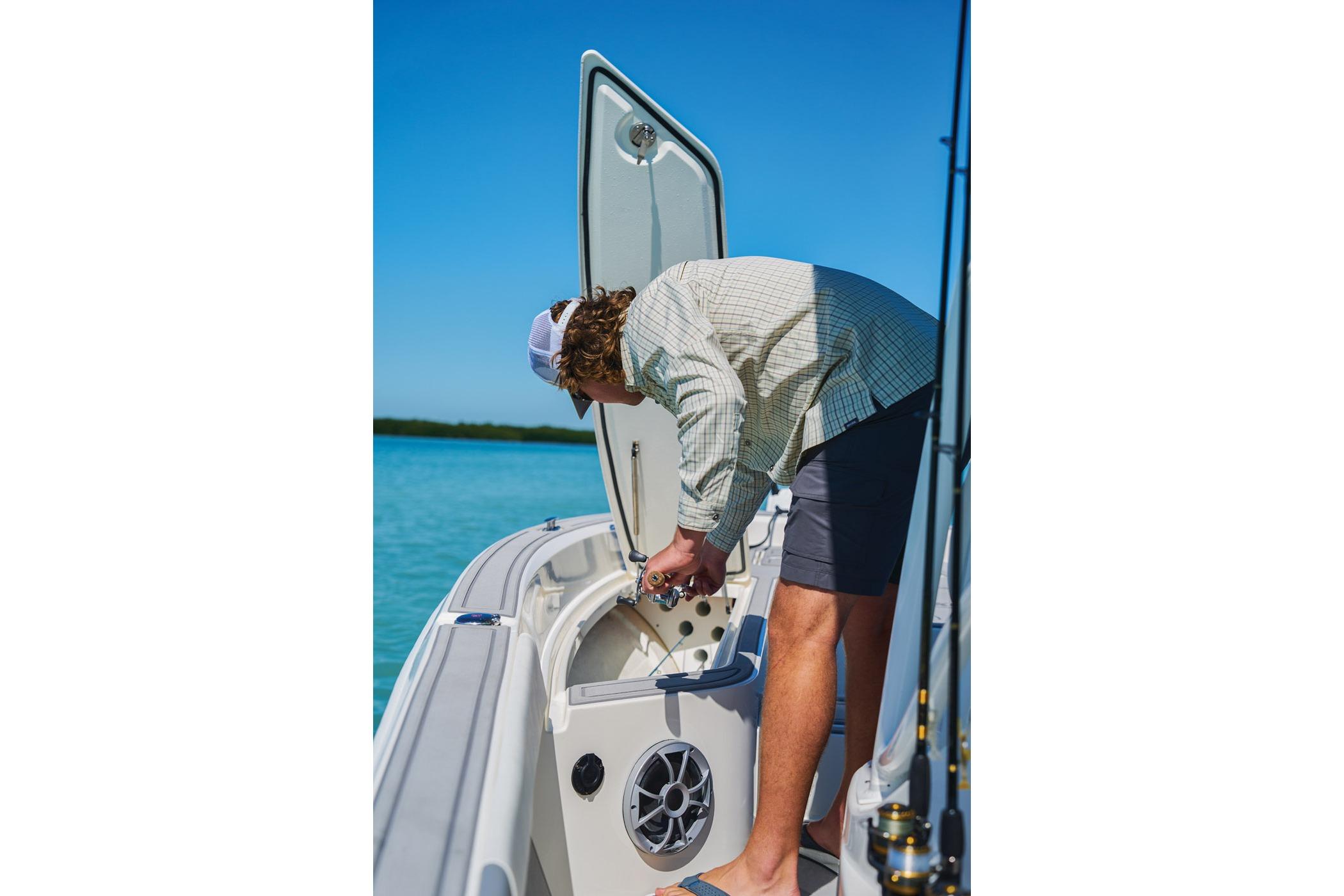 Man inspecting storage on 2026 Mako 24 APEX boat in sunny waters.