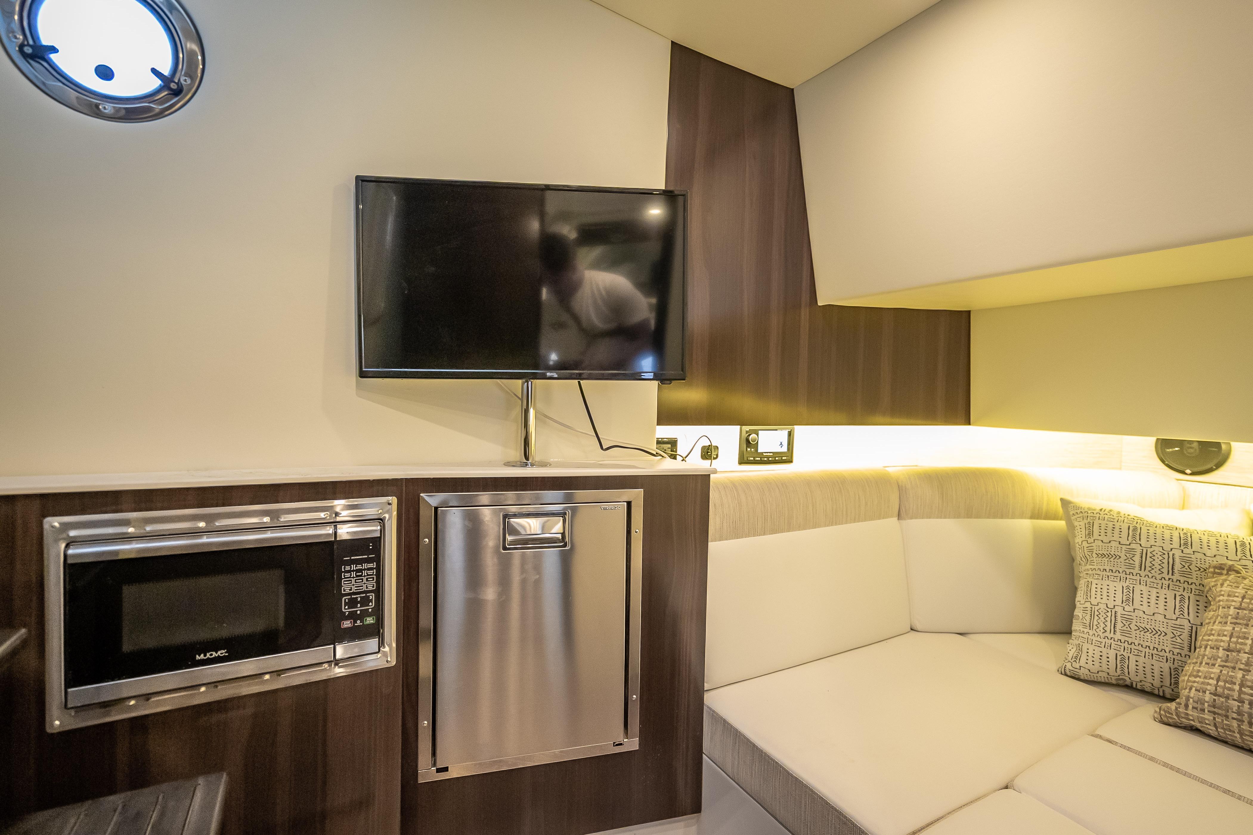 Interior of 2022 Cruisers Yachts 38 GLS OB with TV, microwave, and cozy seating area.