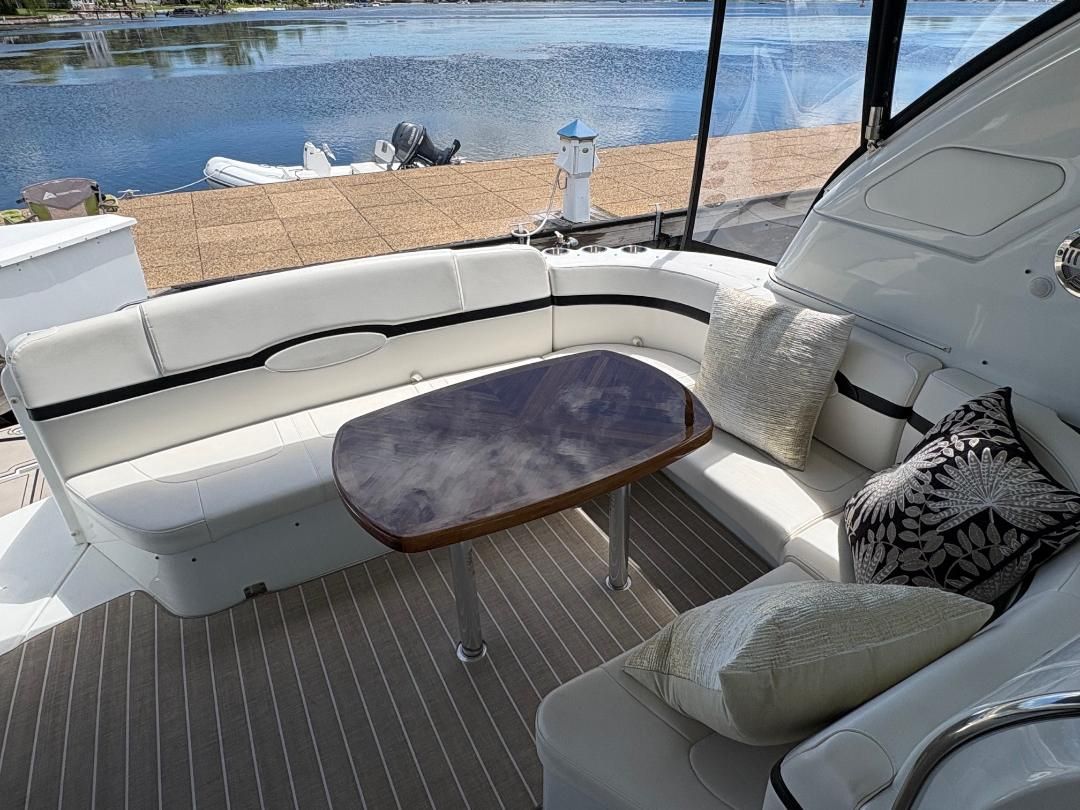 Interior of a luxury yacht with white seating and a wooden table, overlooking the water.