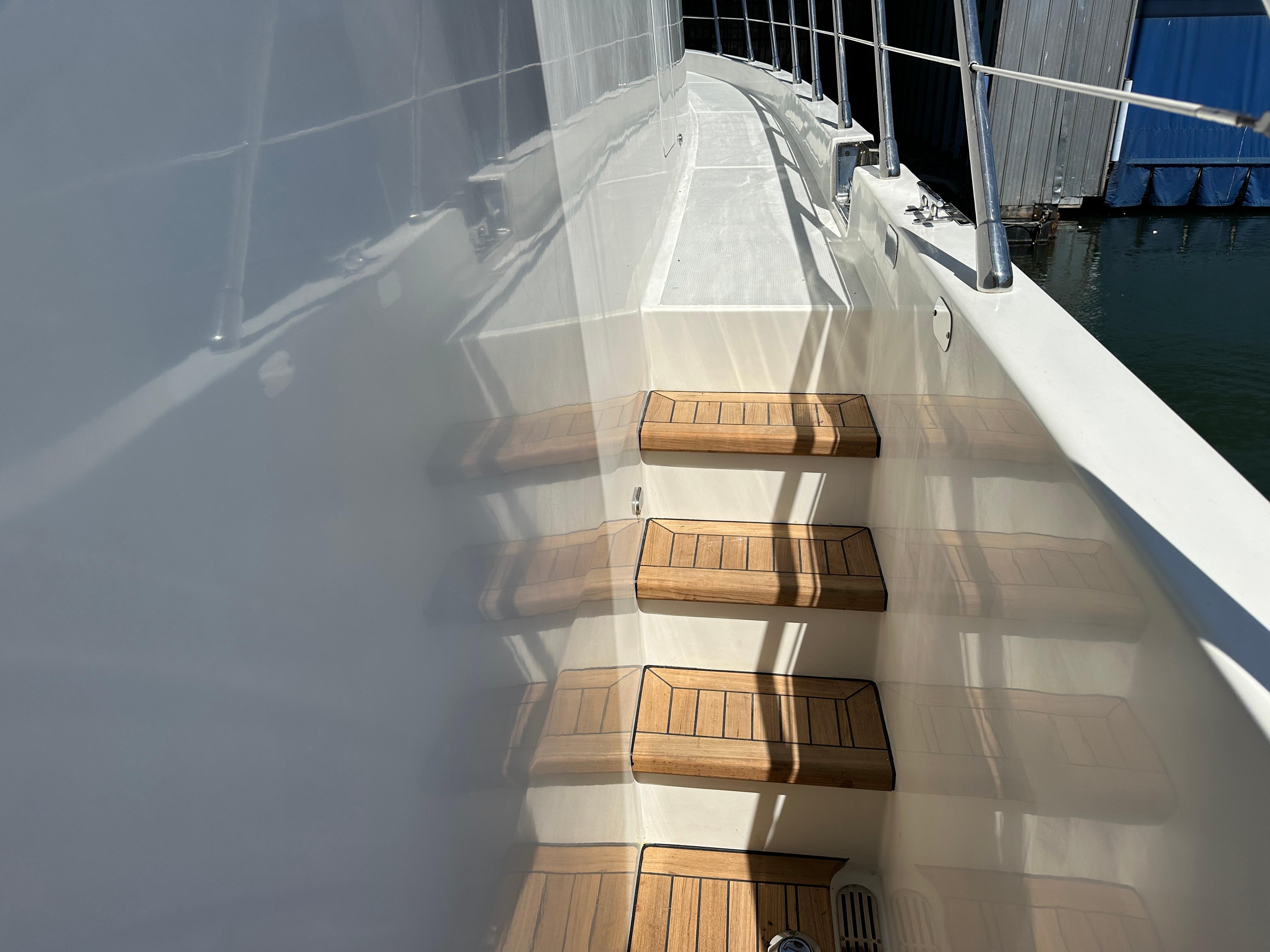Wooden steps on a 2001 Symbol 66 Pilothouse Yacht deck, reflecting sunlight.