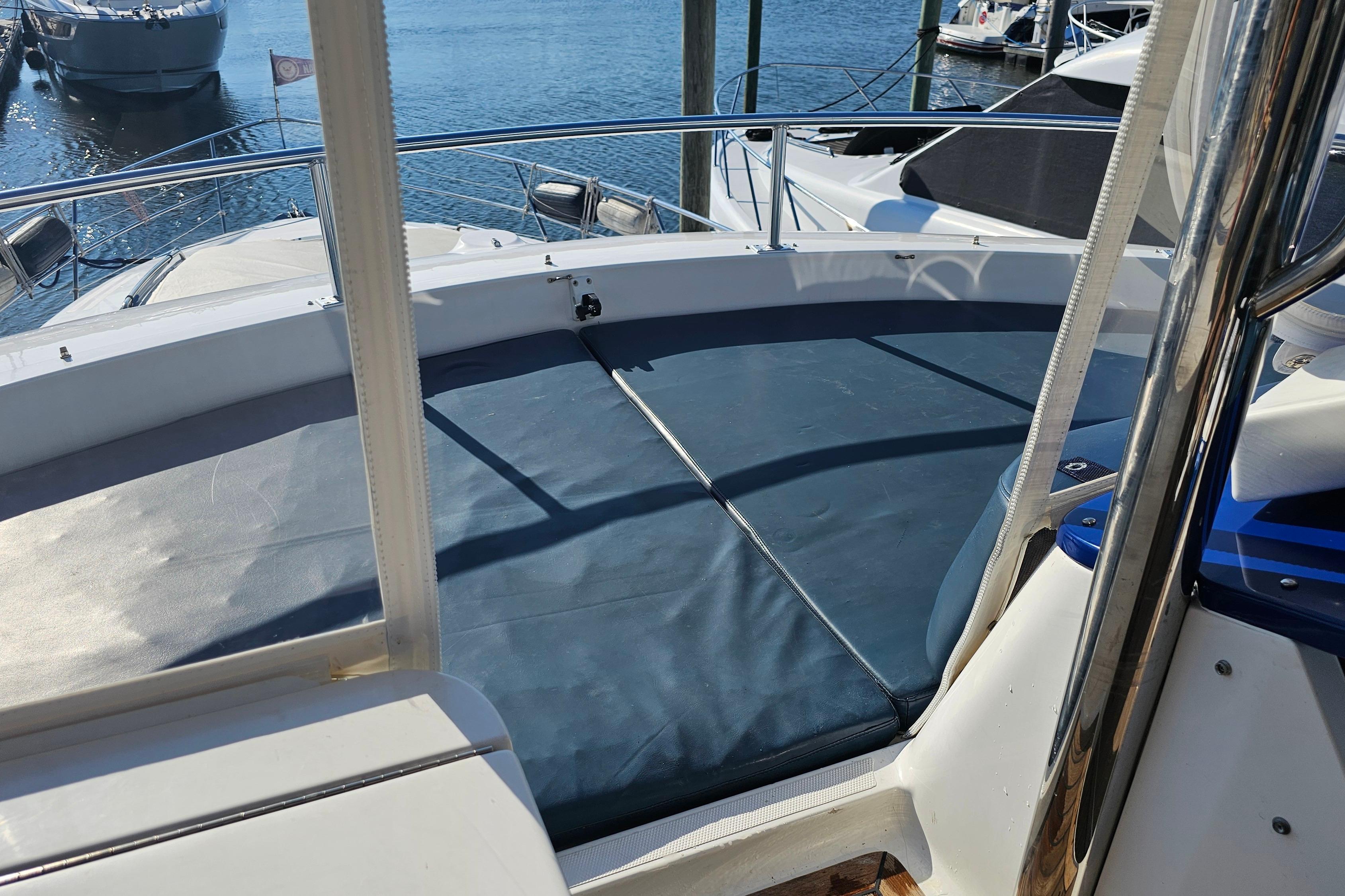 2005 Neptunus 56 Flybridge yacht deck with blue sun pad, docked at marina.