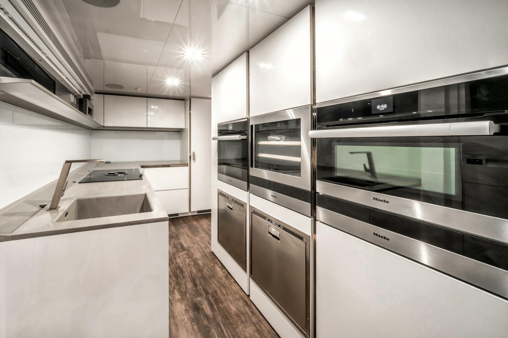 Modern kitchen with sleek appliances, white cabinetry, and wood flooring in a Pearl 95 yacht.