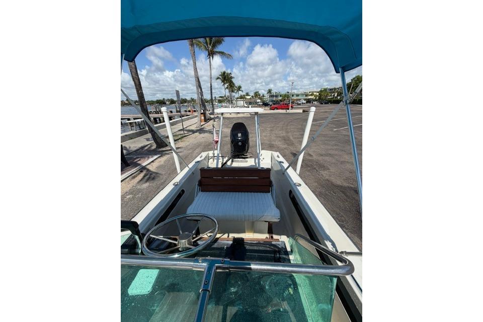 1990 Boston Whaler 17 Newport boat with blue canopy, docked near palm trees.