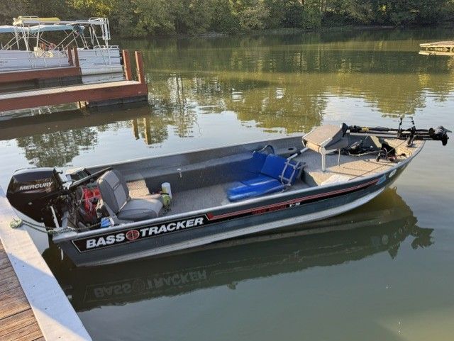 A 1987 Bass Tracker Guide Special V-16 docked at a calm lakeside.