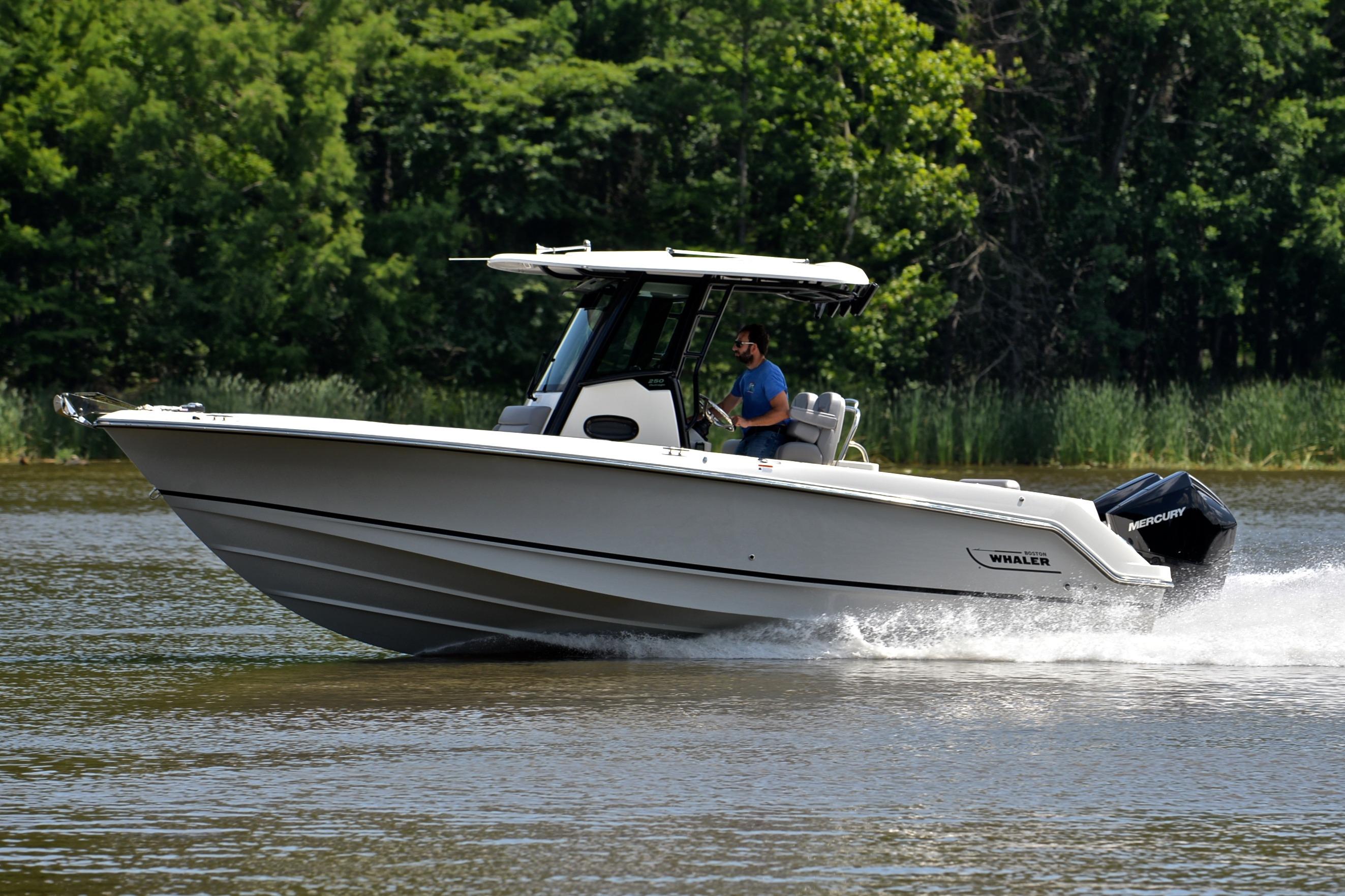 2024 Boston Whaler 250 Outrage cruising on a lake with lush green trees in the background.