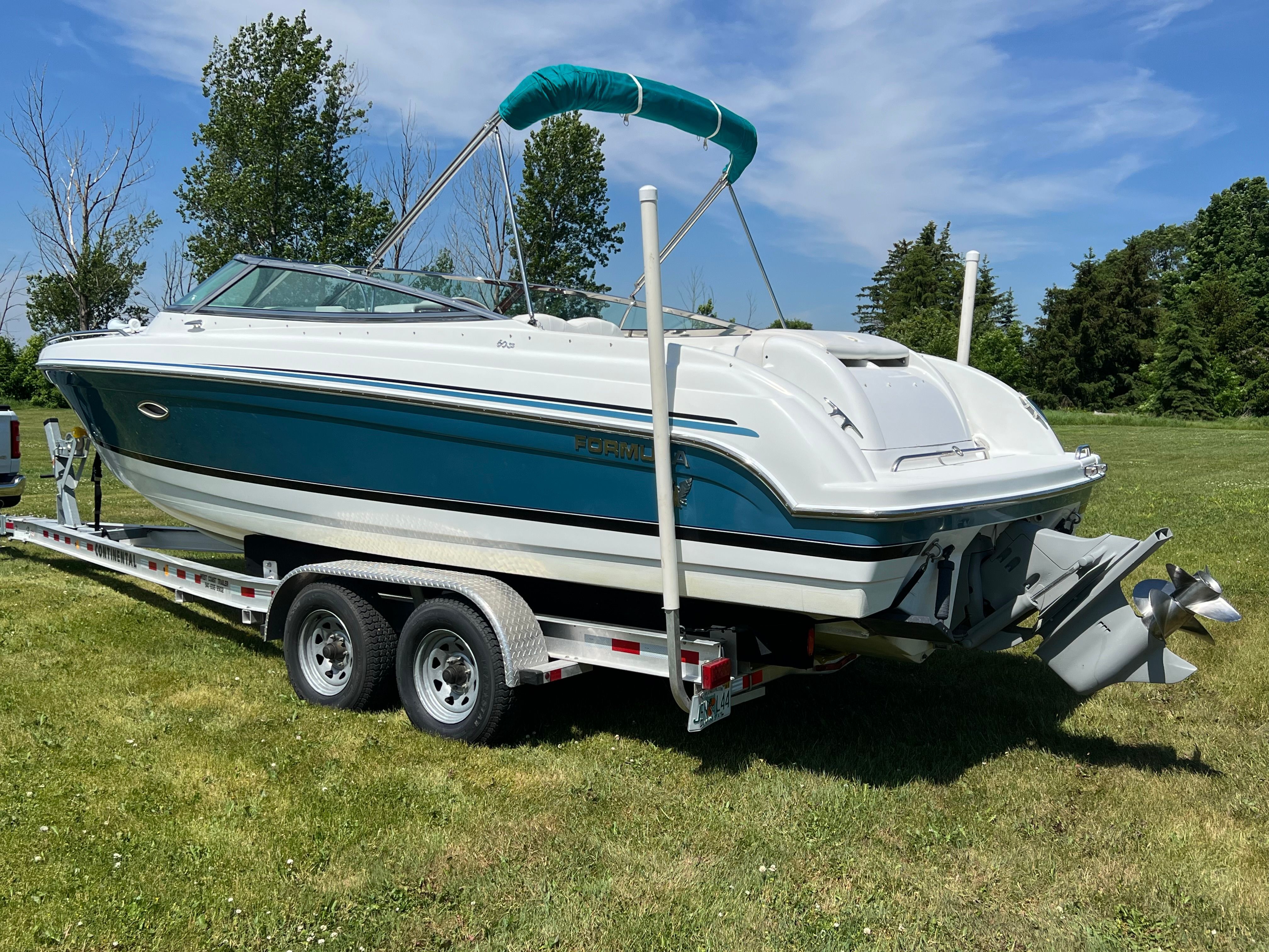 A 2005 Formula 260 Sun Sport boat on a trailer, surrounded by grass and trees.