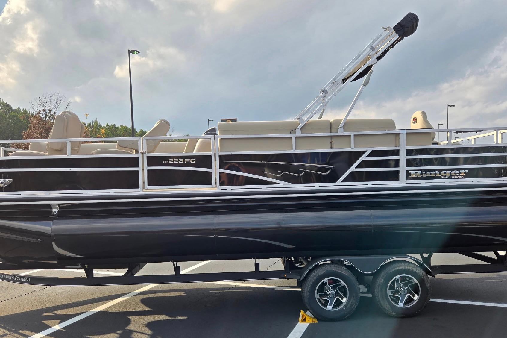 2025 Ranger Reata 223FC pontoon boat on trailer, parked in a lot under cloudy sky.