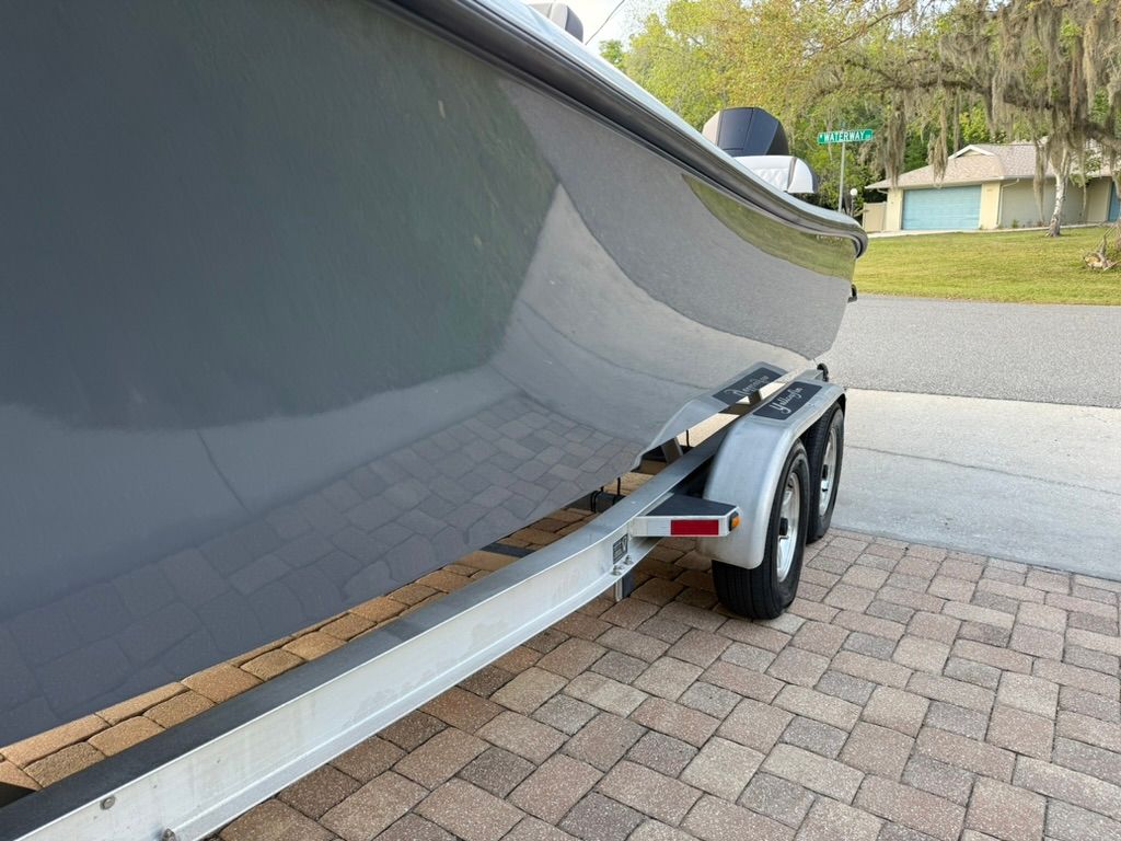 A gray boat on a trailer is parked on a paved driveway.