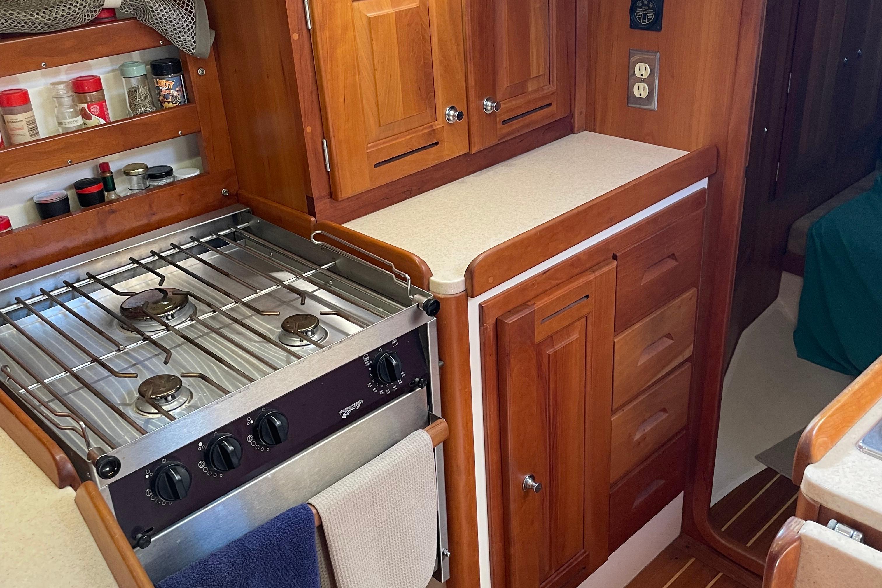 Wooden yacht kitchen with stove, spice rack, and cabinetry in a 2004 Tartan 3700.