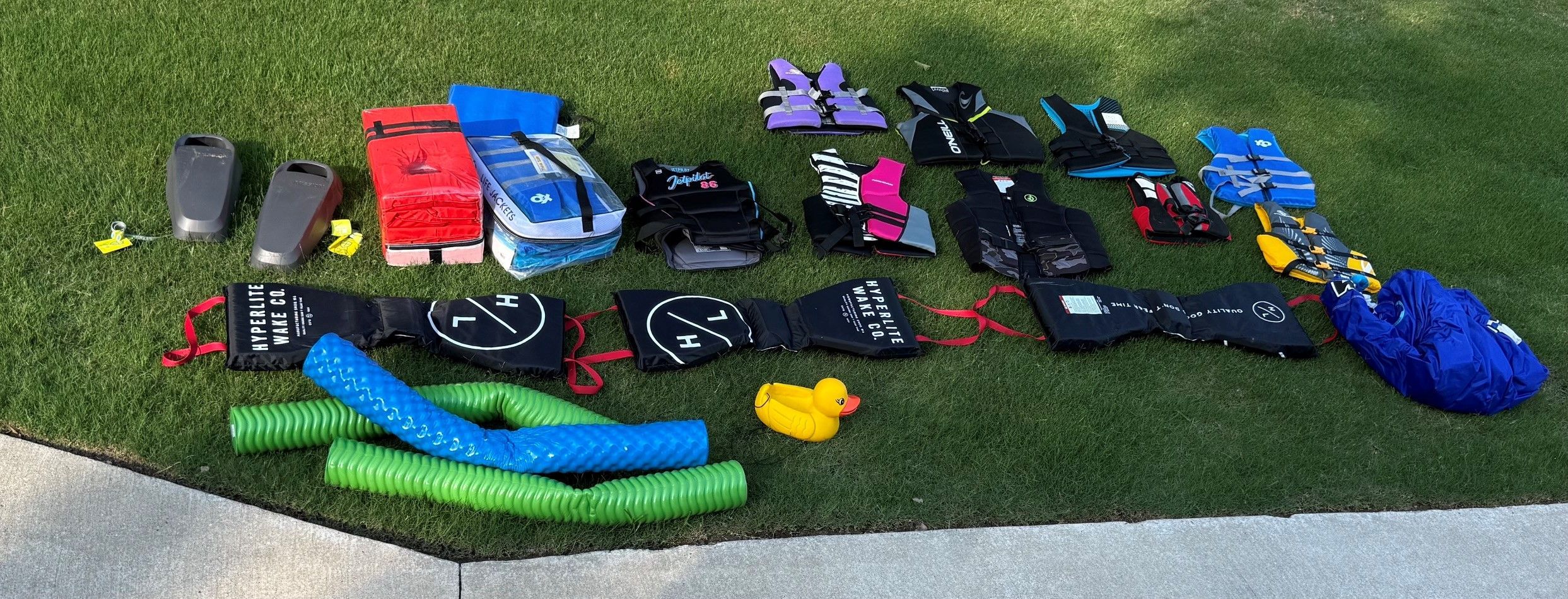 Various life jackets and water sports gear laid out on grass.