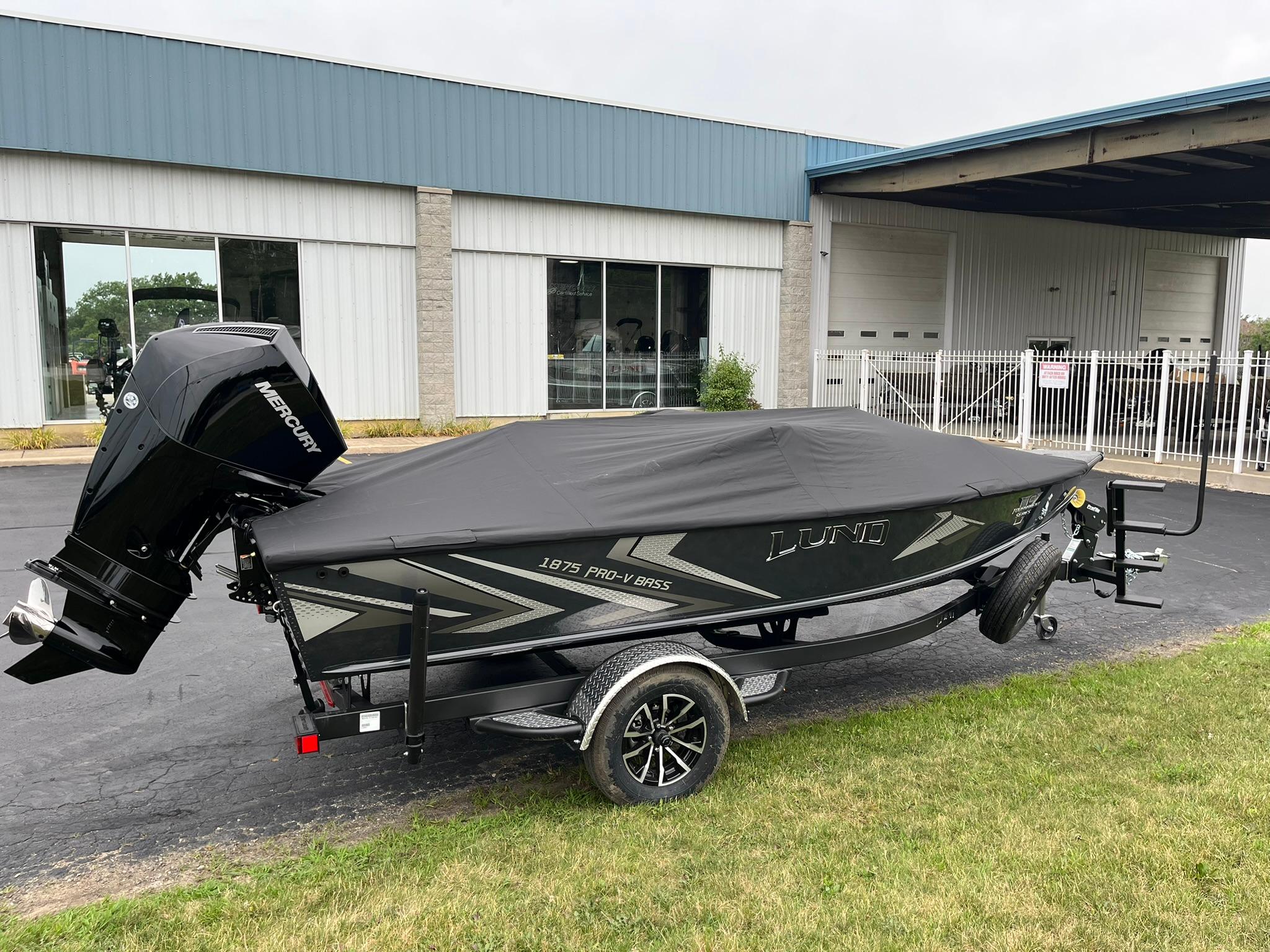2026 Lund 1875 Pro-V Bass XS boat with cover and Mercury engine, parked outside.
