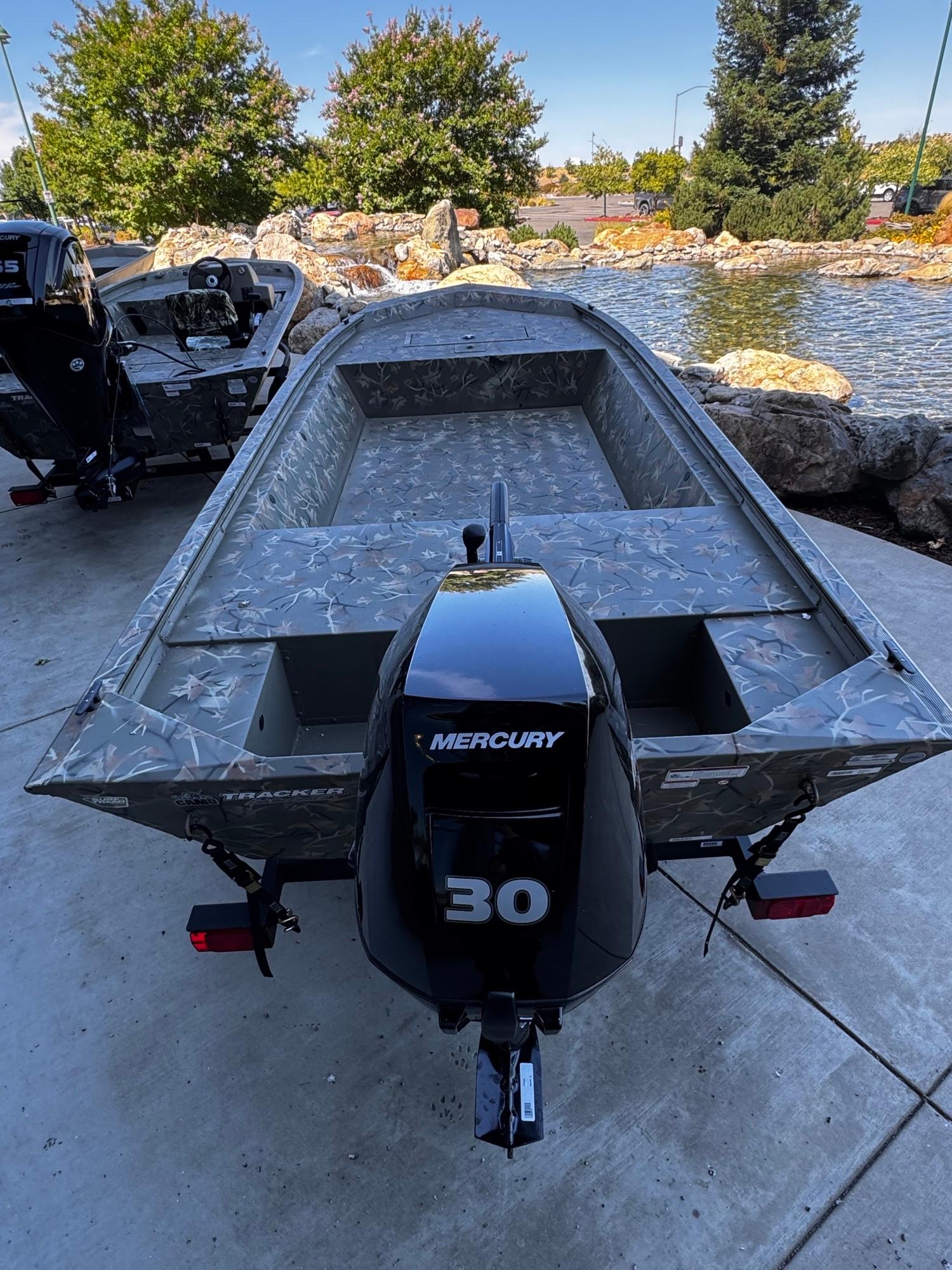 2025 Tracker Grizzly 1648 Jon boat with Mercury 30 engine, parked near a pond.