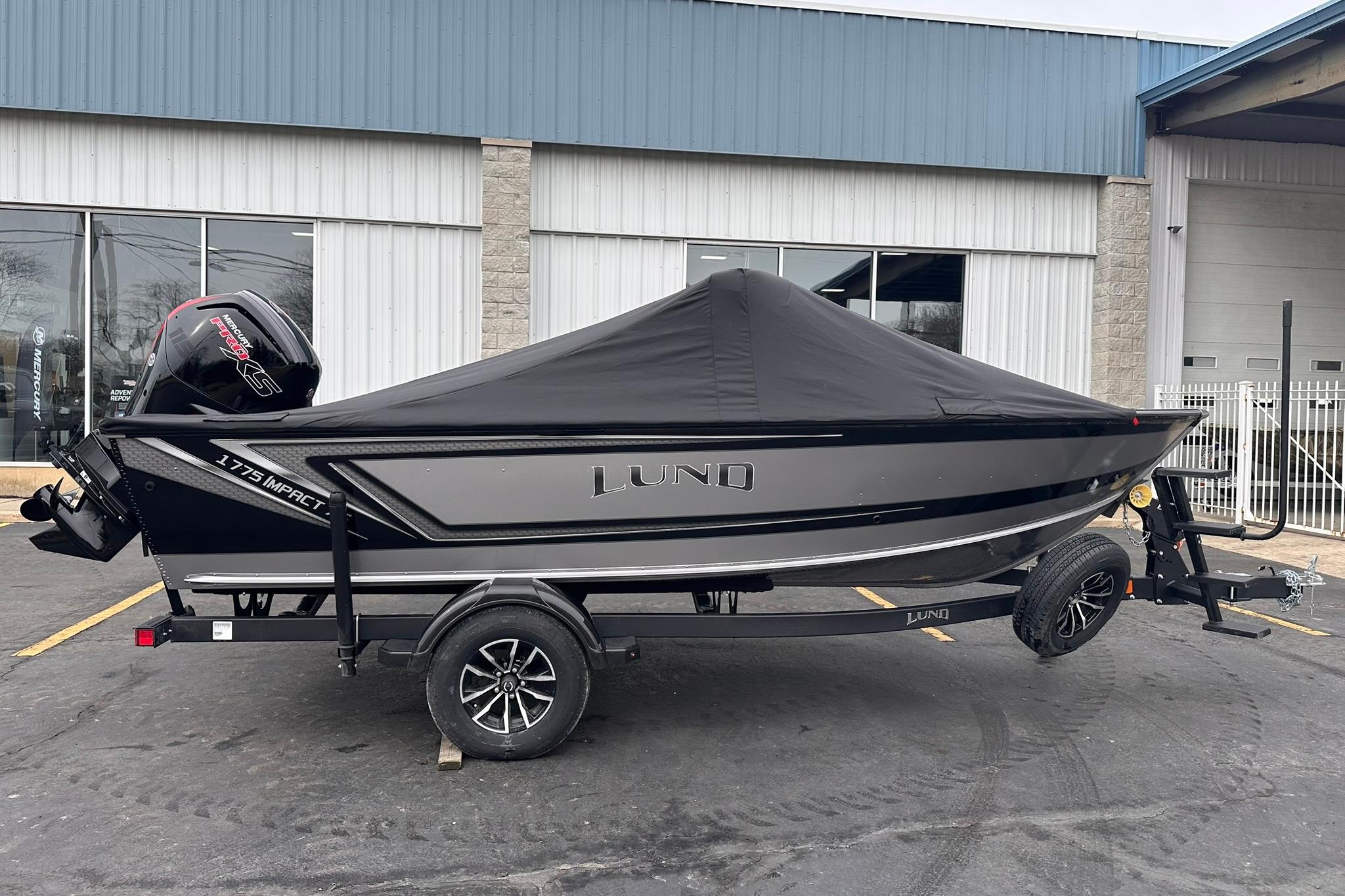 2026 Lund 1775 Impact XS Sport boat with cover on trailer, parked outside a building.
