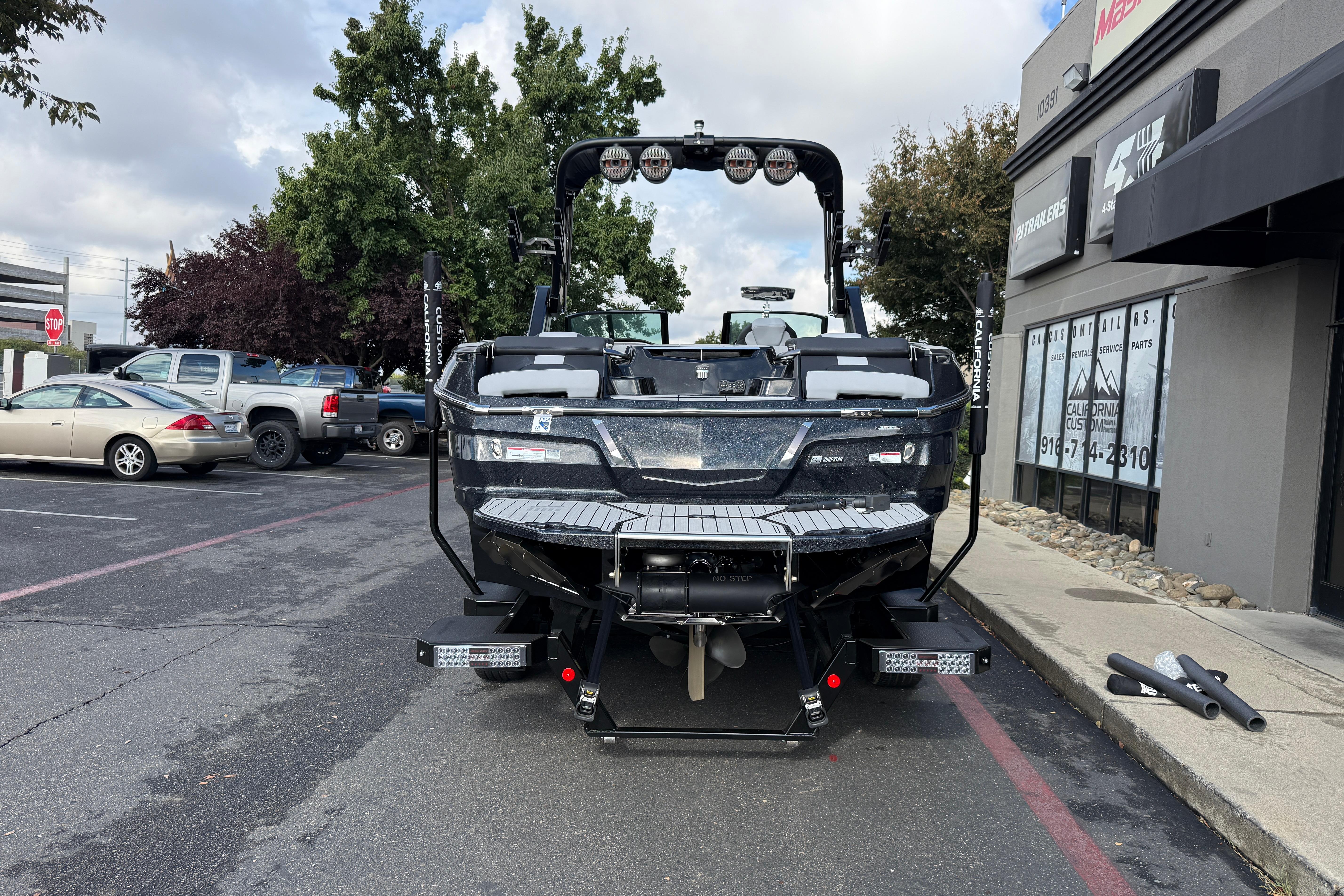 2024 MasterCraft X24 boat parked in a lot, rear view with trees and buildings.