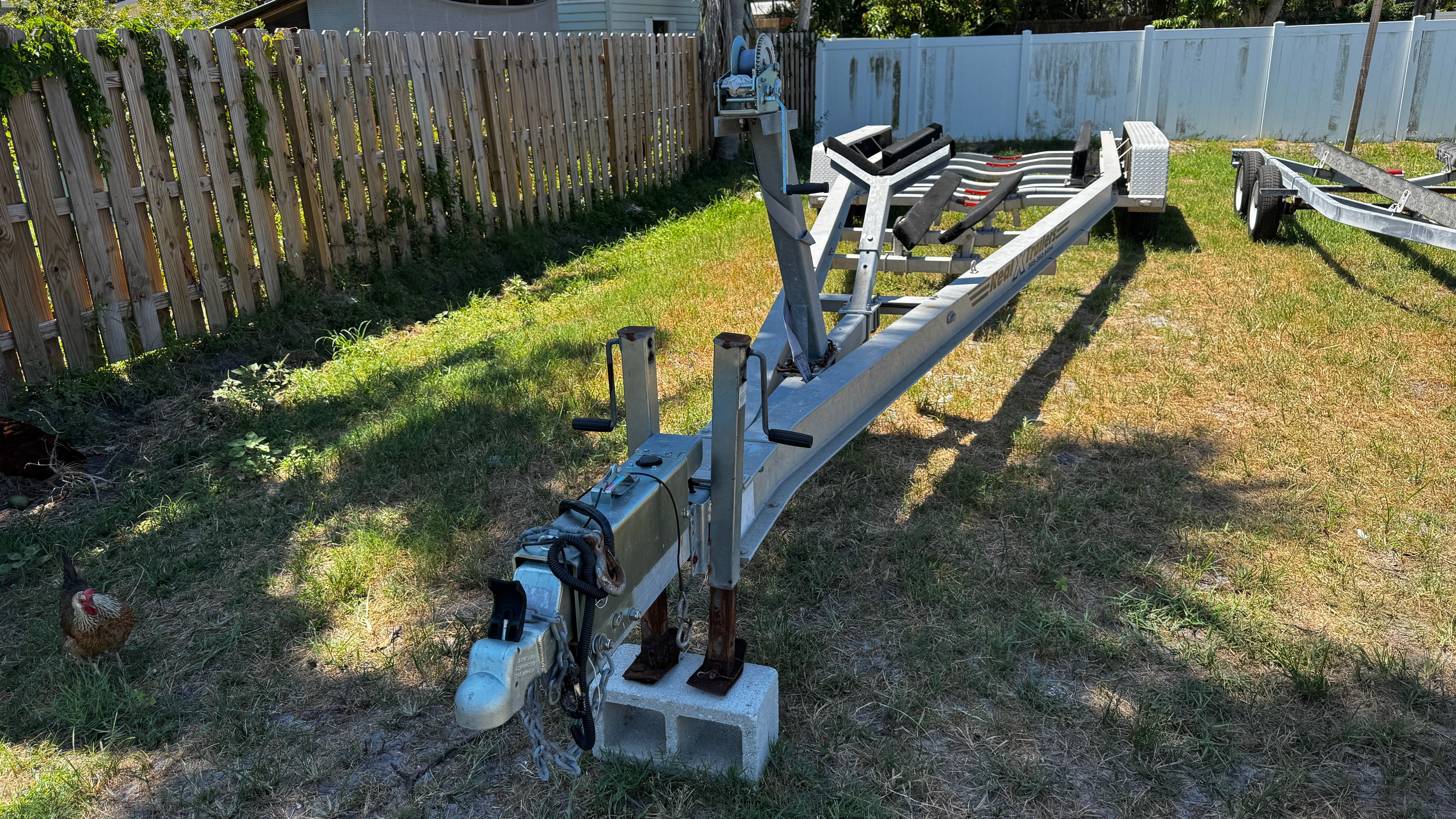 Boat trailer on grass with wooden fence in the background.
