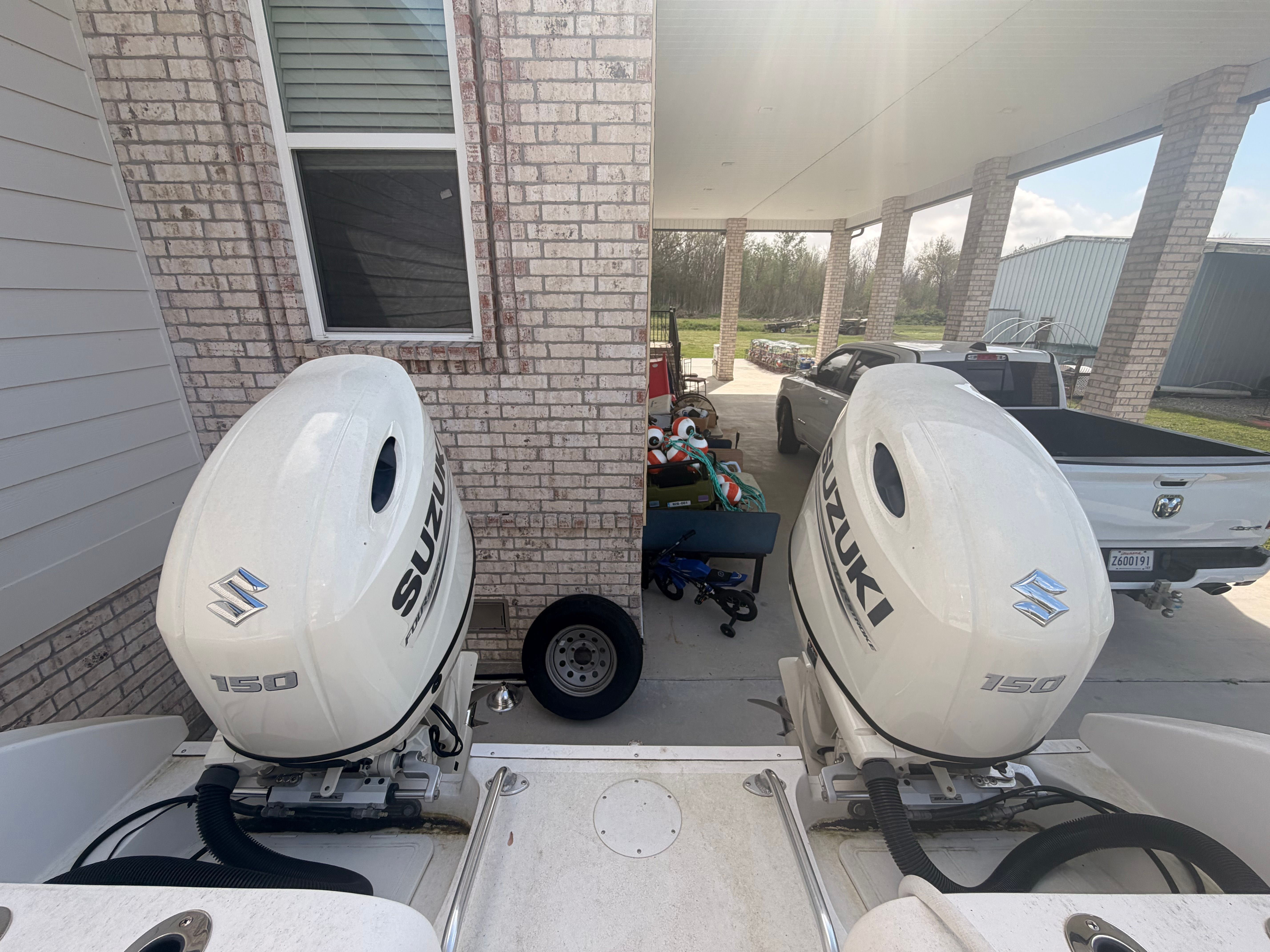 Two Suzuki outboard motors on a boat parked in a driveway next to a house.