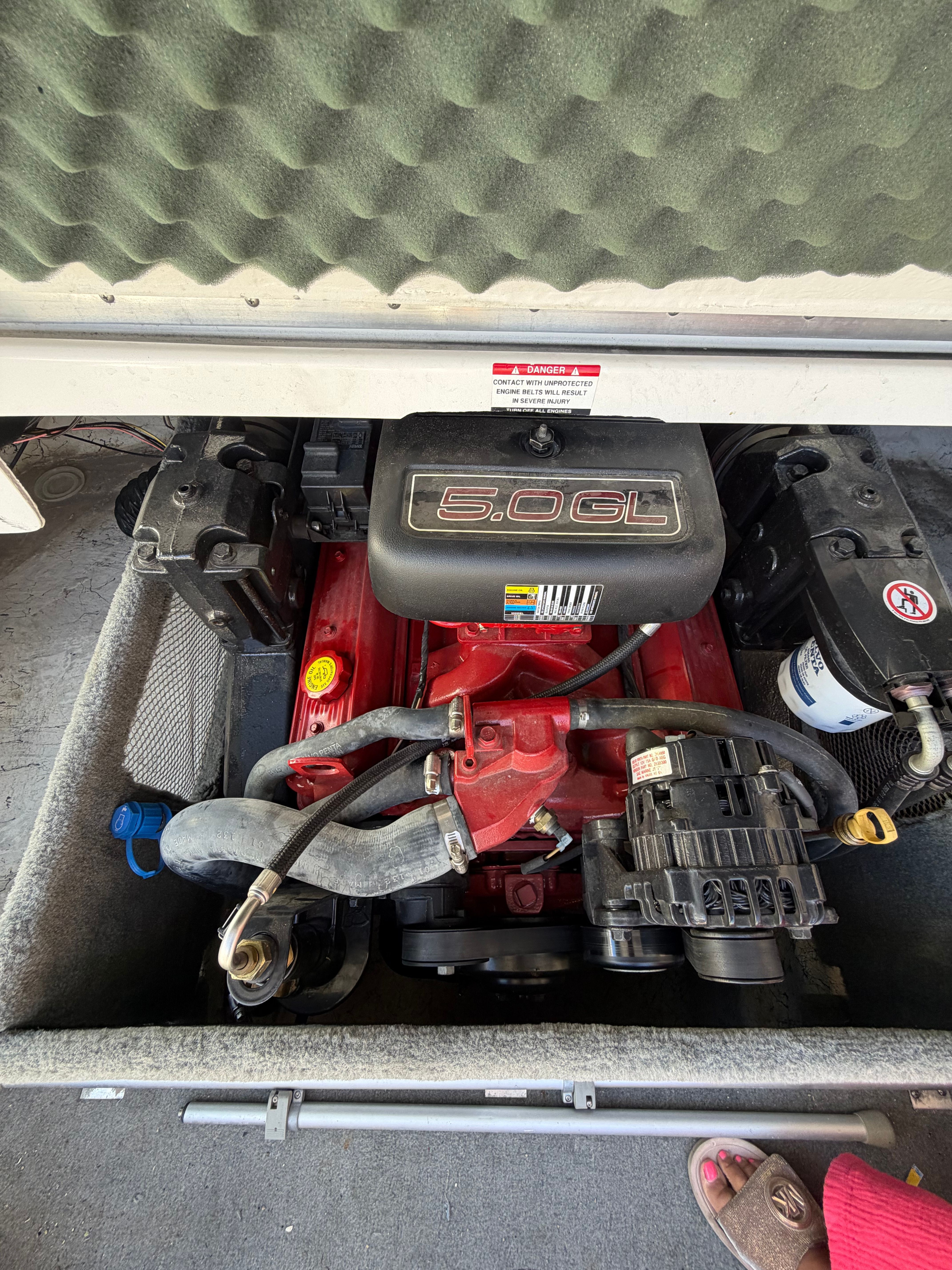 A boat engine with a red casing and black cover, surrounded by hoses and cables.
