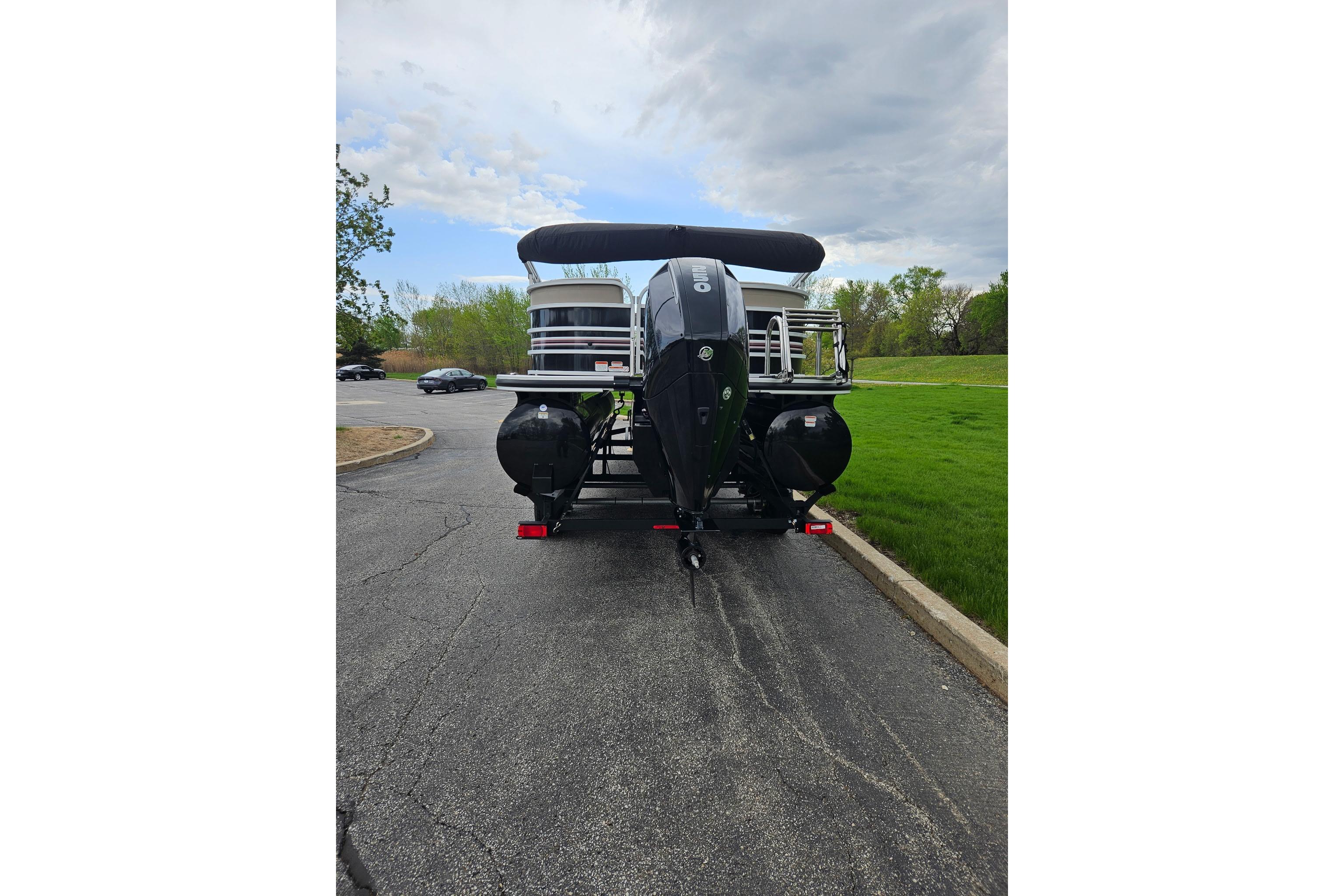 2023 Ranger Reata 243C pontoon boat on trailer, parked in a lot with cloudy sky.