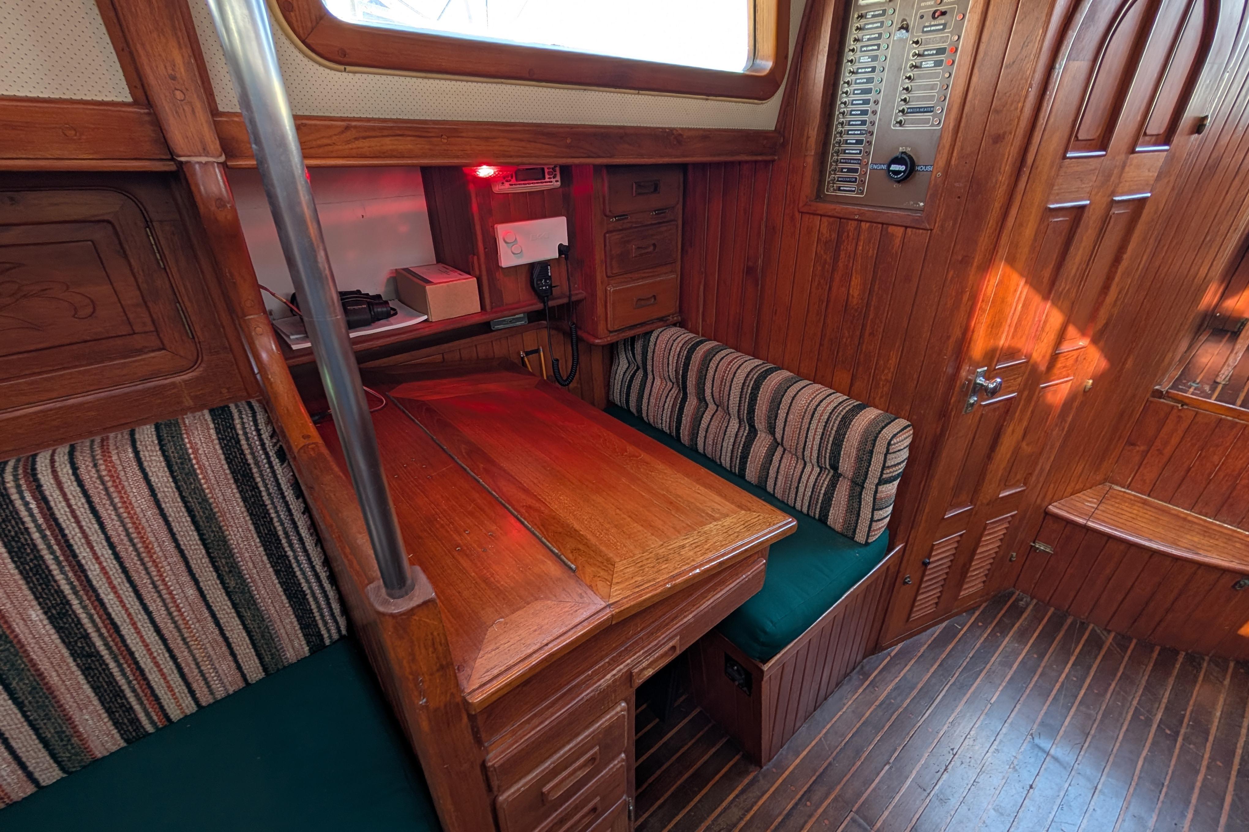 Cozy wooden interior of 1983 Robert Perry 41 sailboat with striped seating and navigation area.