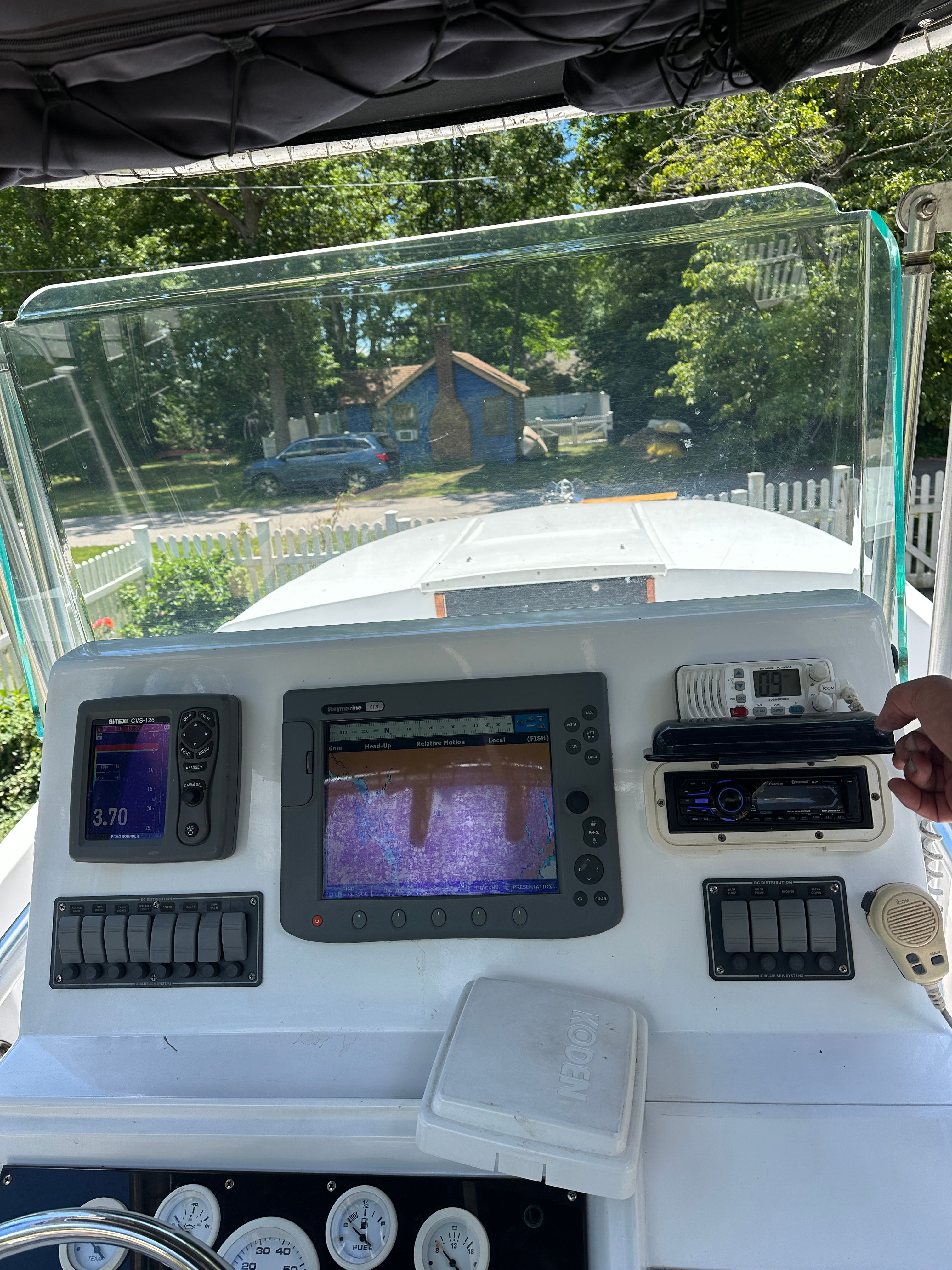The image shows a boat's cockpit with modern navigation equipment and a steering wheel.