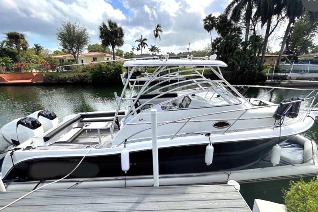 2006 Pro-Line 32 Express boat docked by a scenic waterfront with palm trees.
