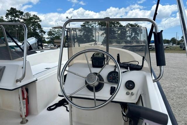 1989 Henry O 150 Dual Console boat steering wheel and dashboard under a partly cloudy sky.