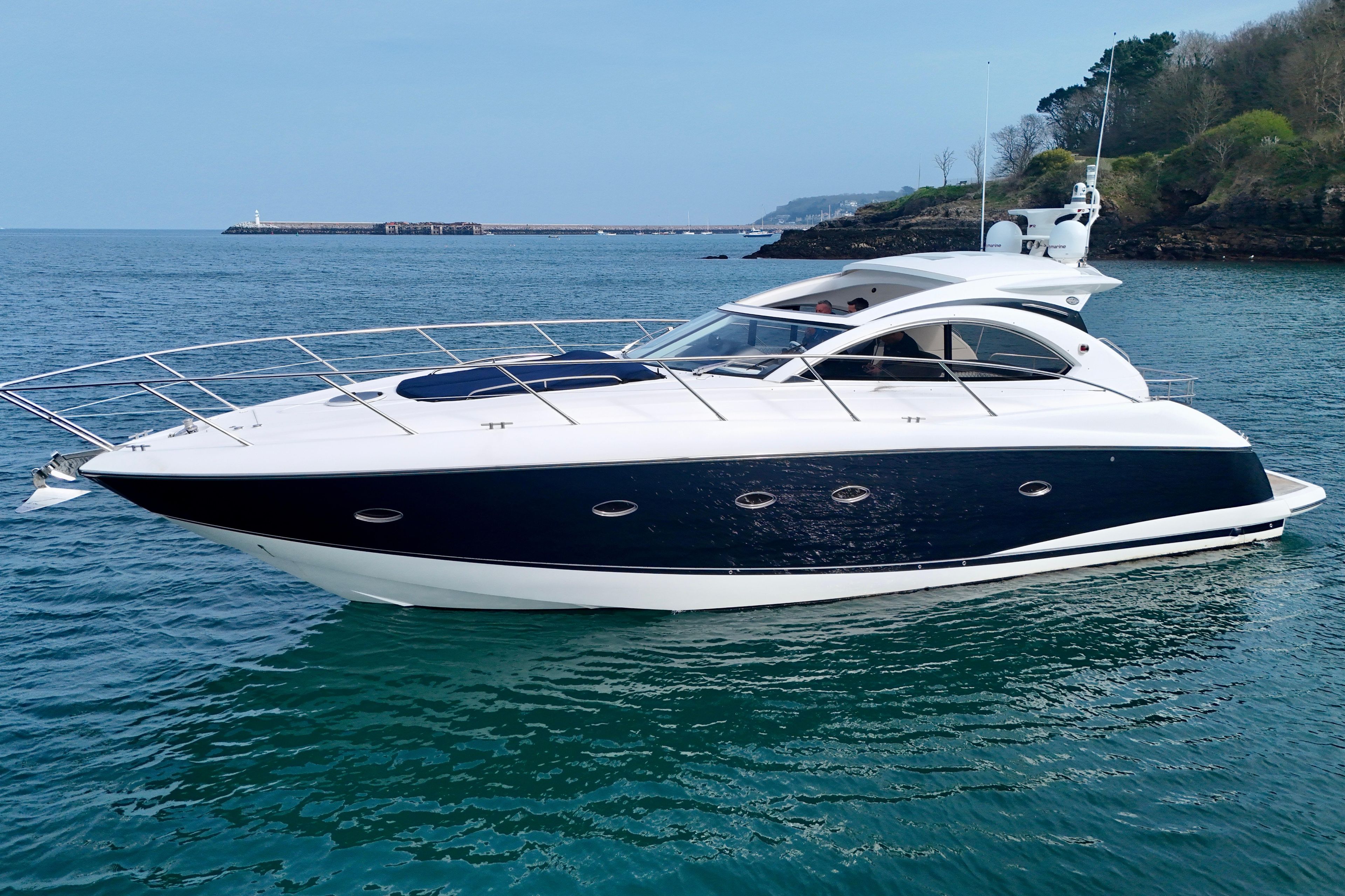2007 Sunseeker Portofino 47 yacht cruising on calm blue waters near a rocky coastline.