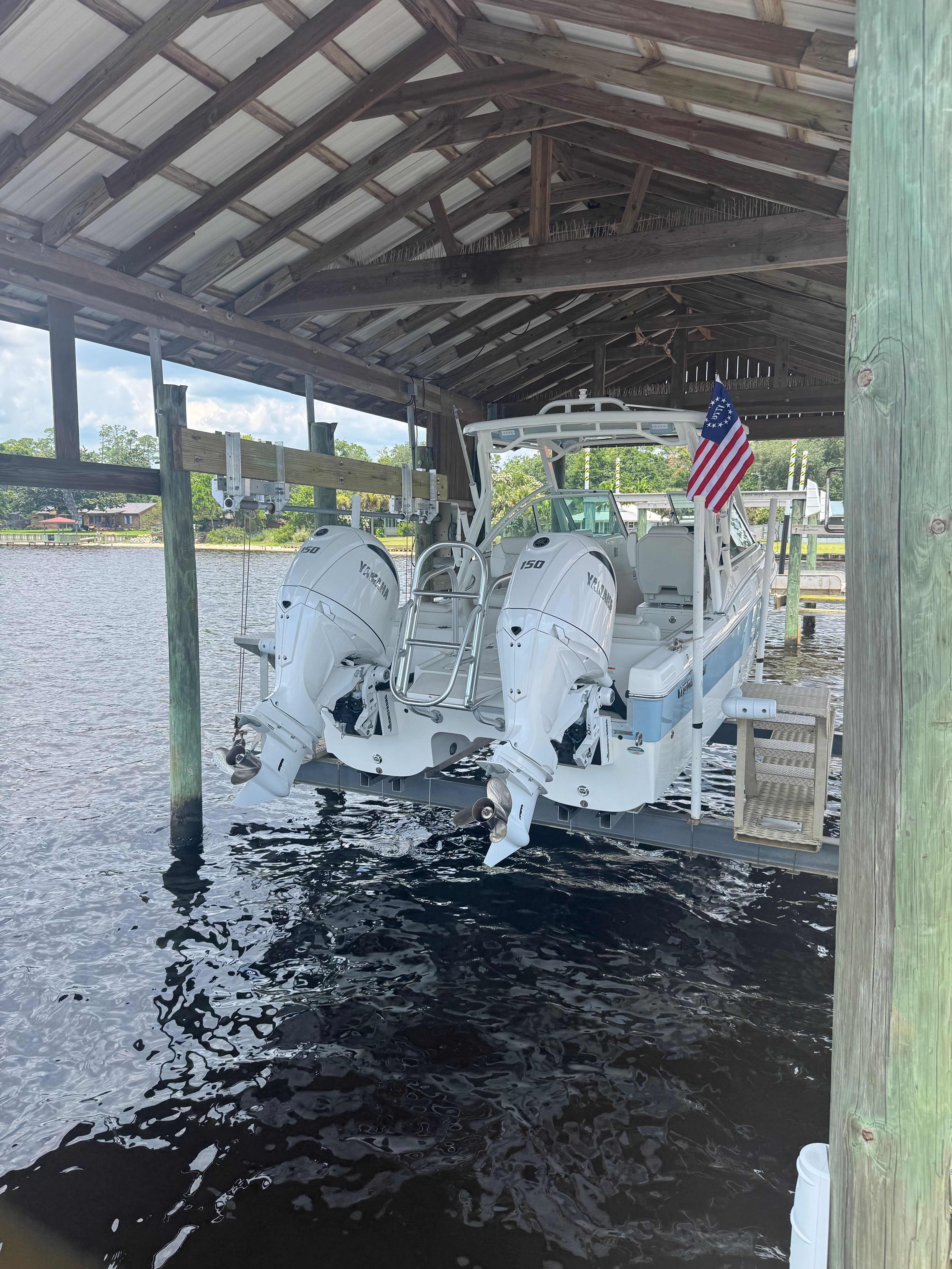 A 2025 World Cat 230 DC boat under a covered dock with two outboard engines.