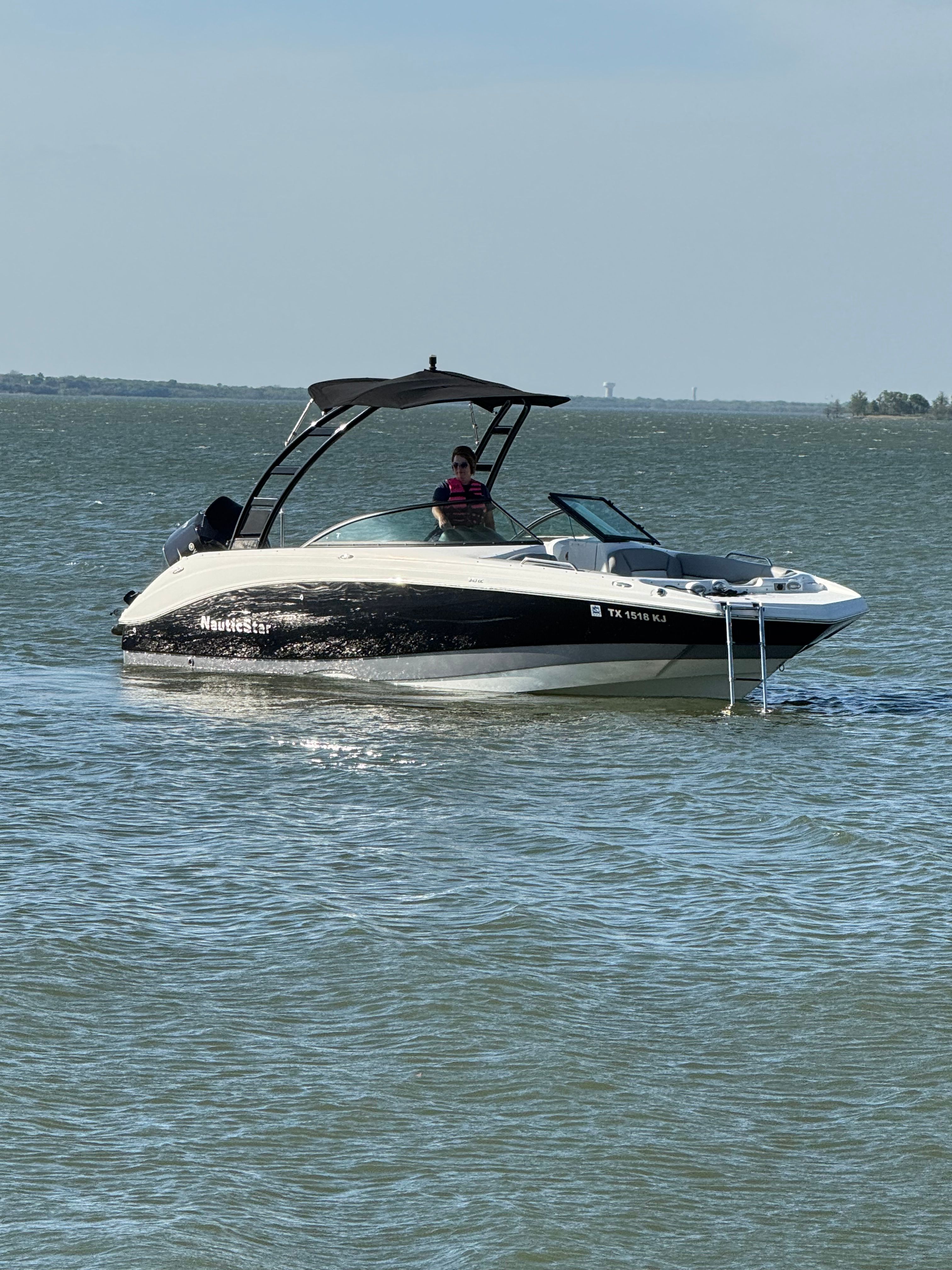 A 2021 NauticStar 243 DC boat on the water with a black canopy.