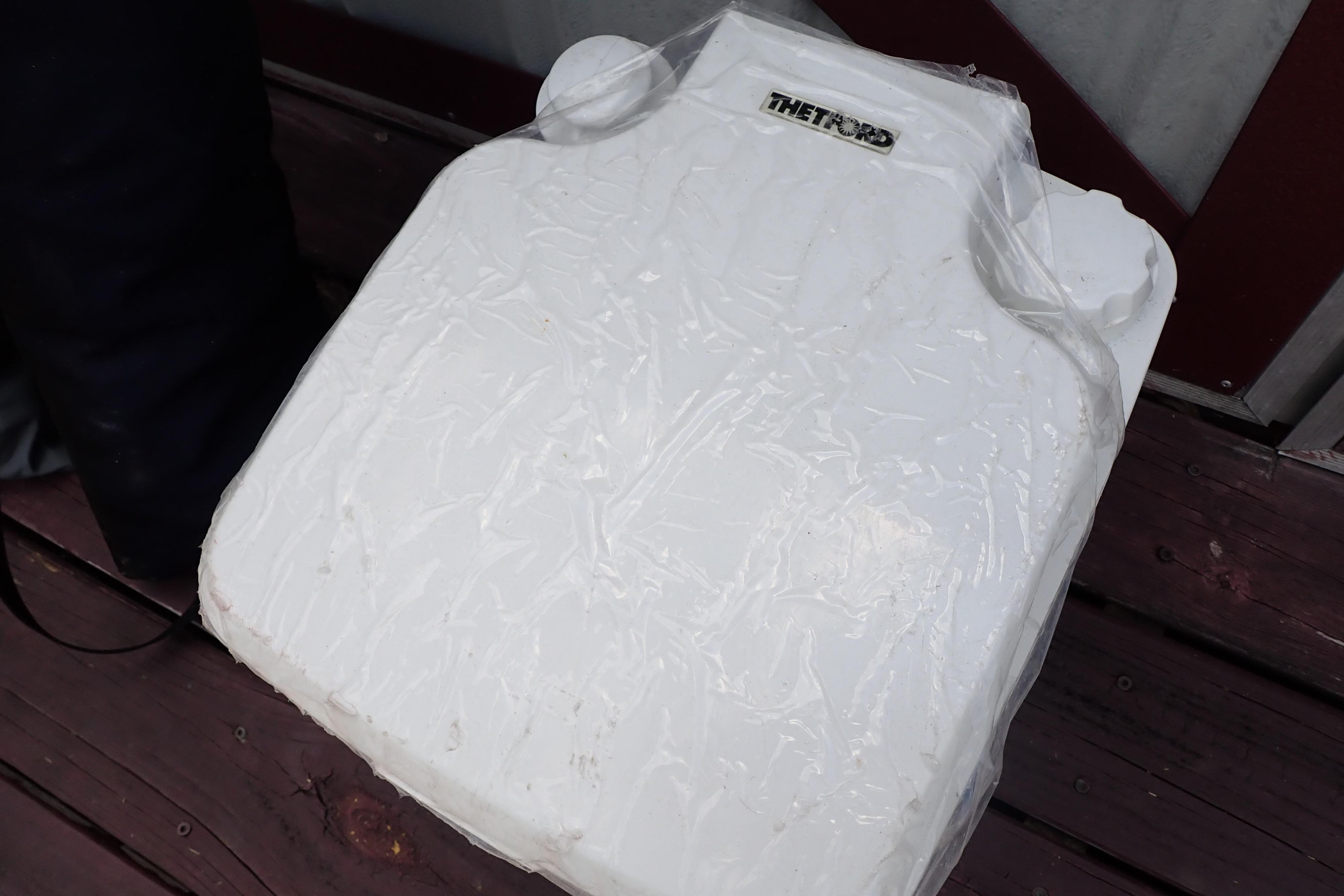 White Thetford portable toilet on wooden deck, wrapped in plastic.