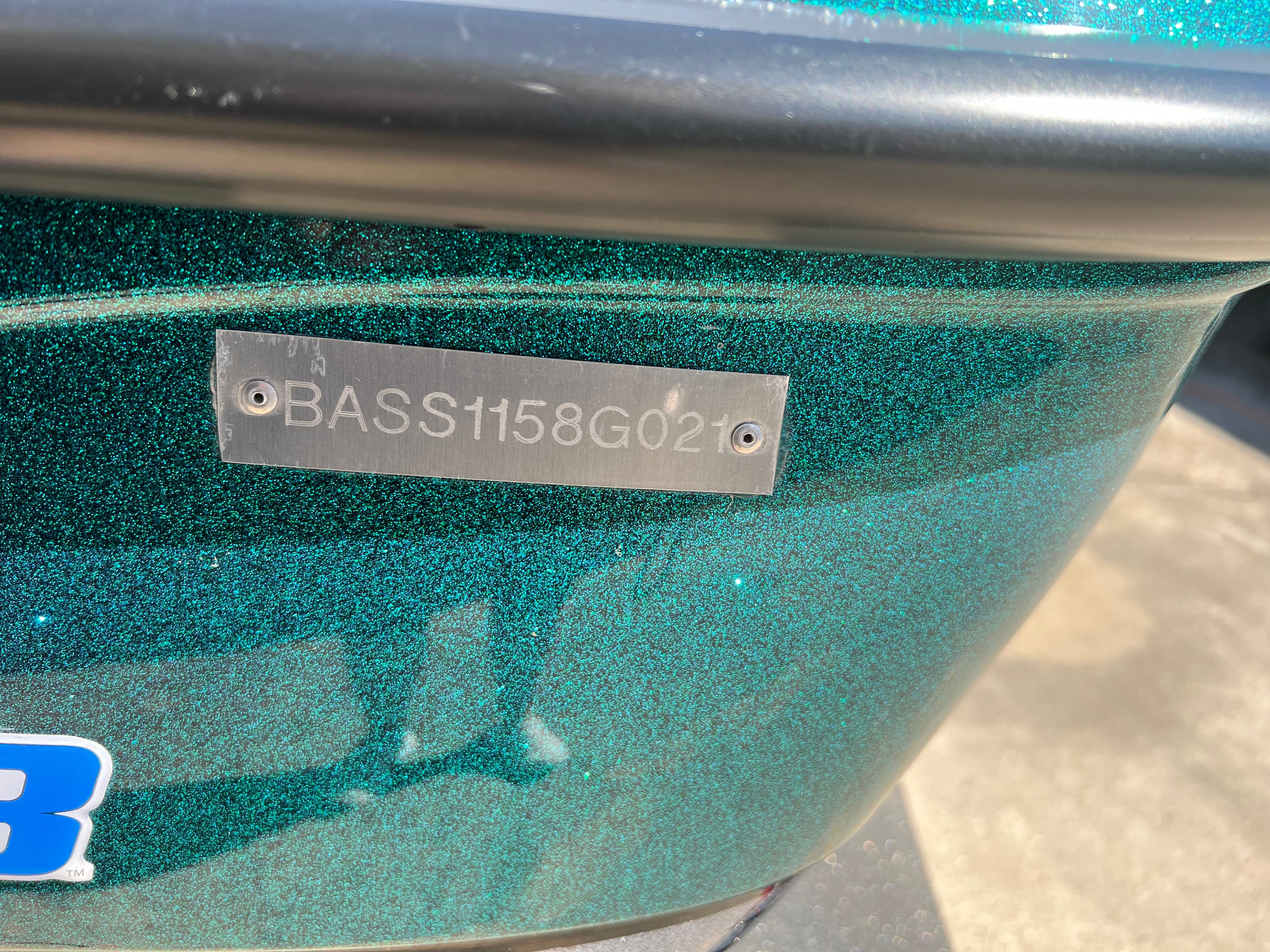 Close-up of a green boat hull with a metal plaque displaying "BASS1158G021."