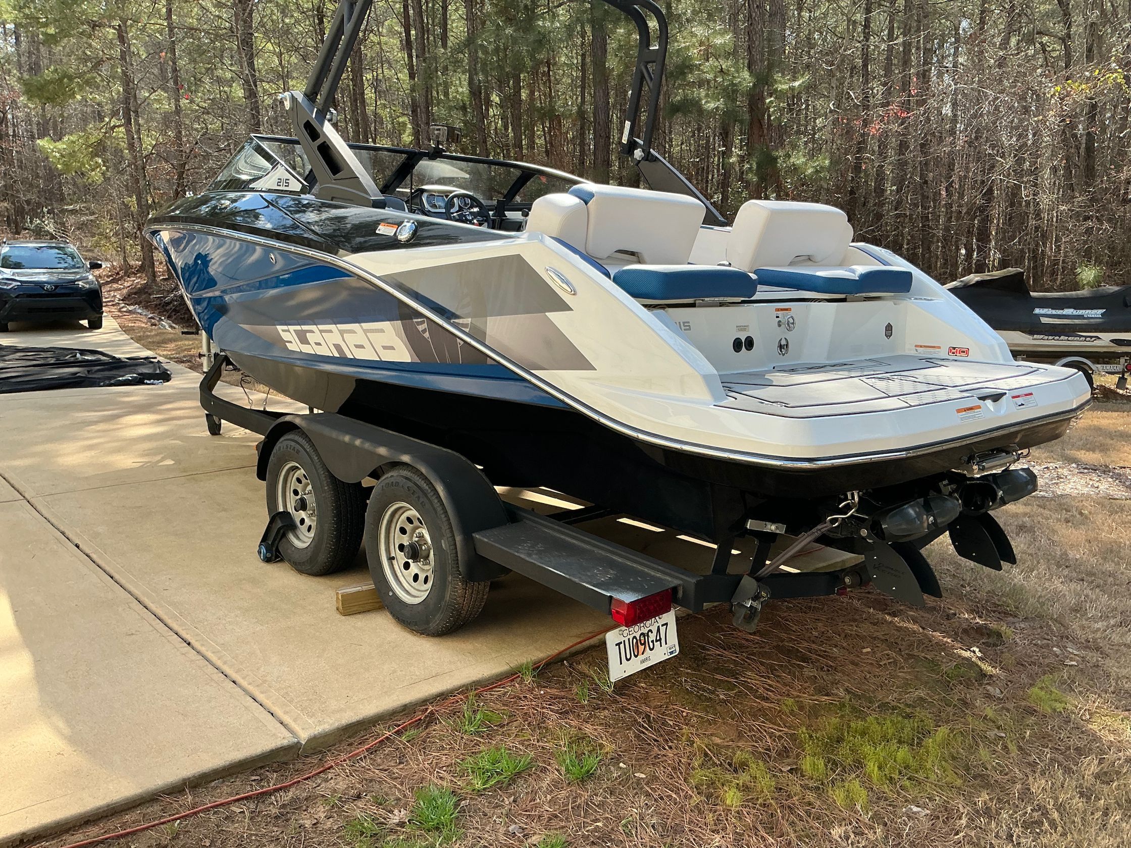 2021 Scarab 215 ID boat on trailer parked in wooded area.