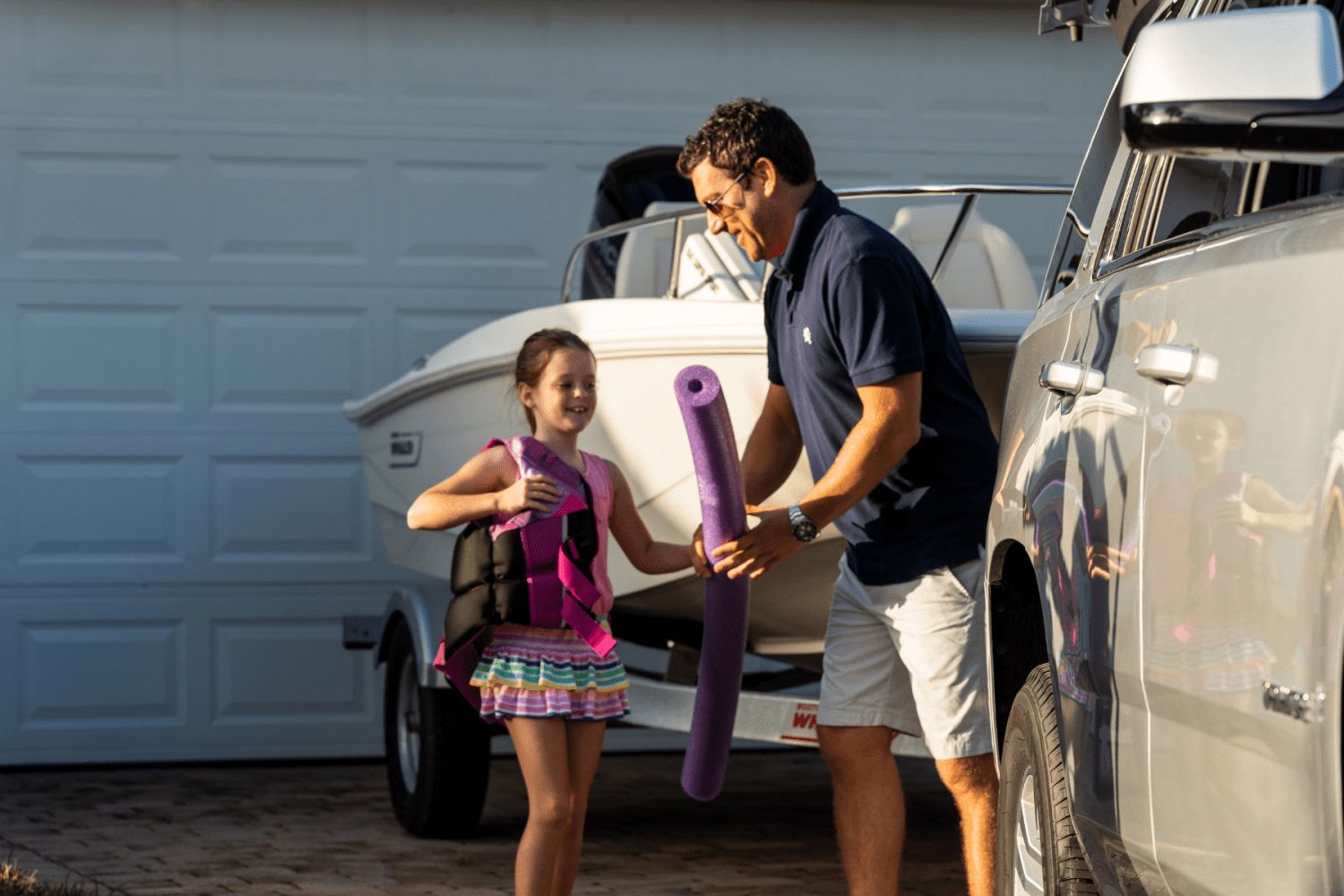 A man and child prepare for a boat trip with pool noodles and life jackets.