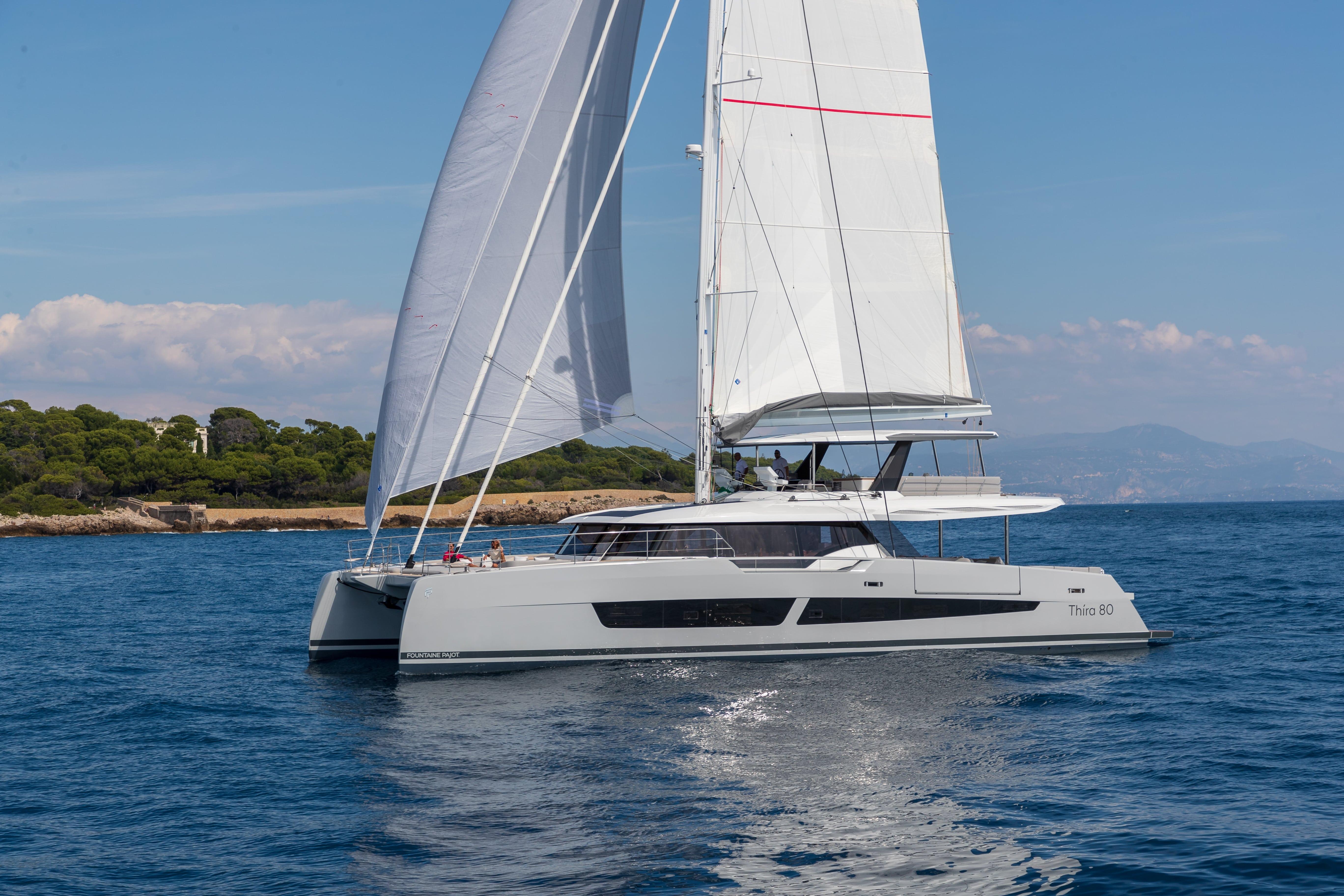2025 Fountaine Pajot Thira 80 sailing on calm blue waters near a scenic coastline.