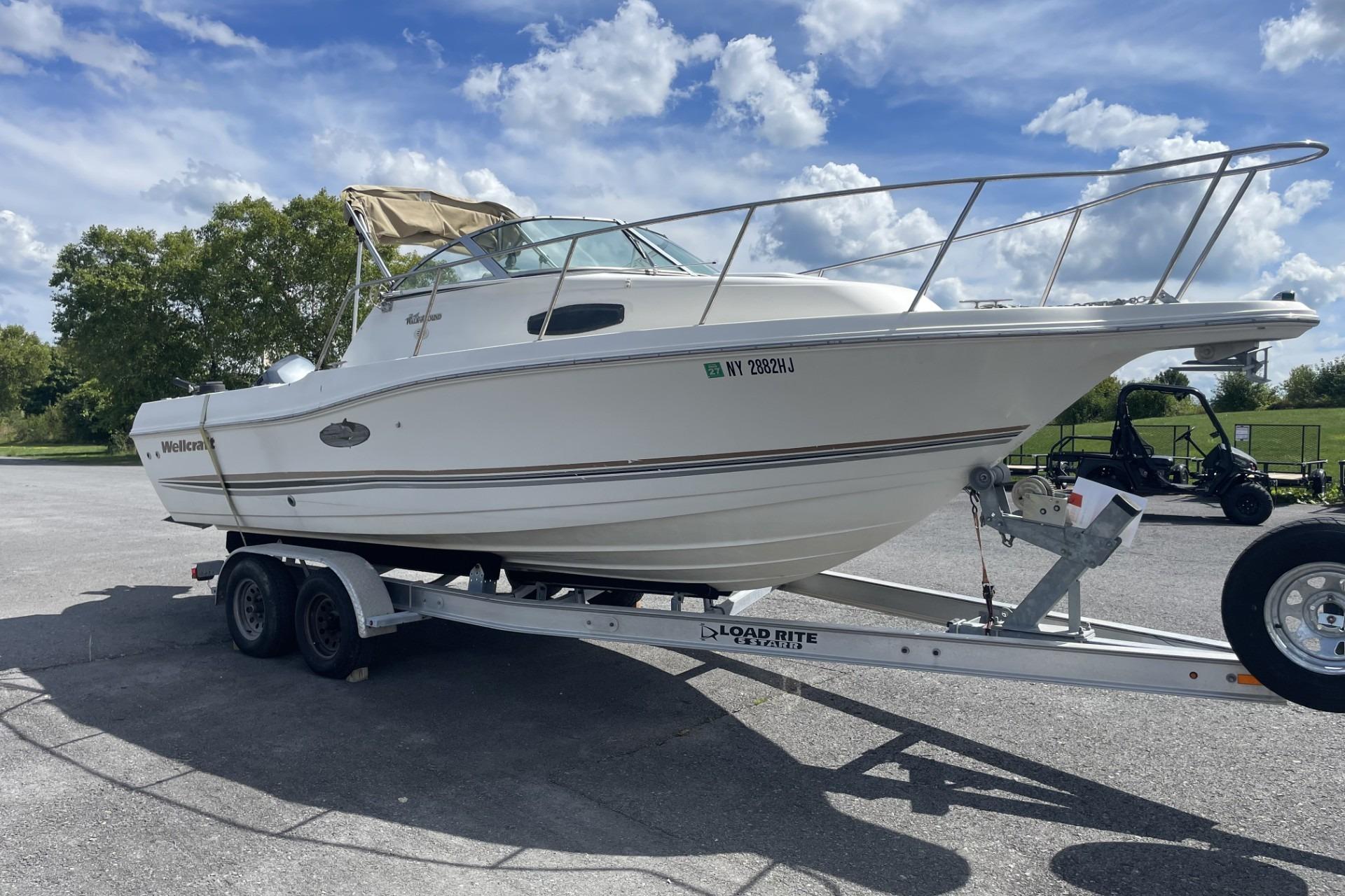 2002 Wellcraft 24 Walkaround boat on trailer under a clear blue sky.