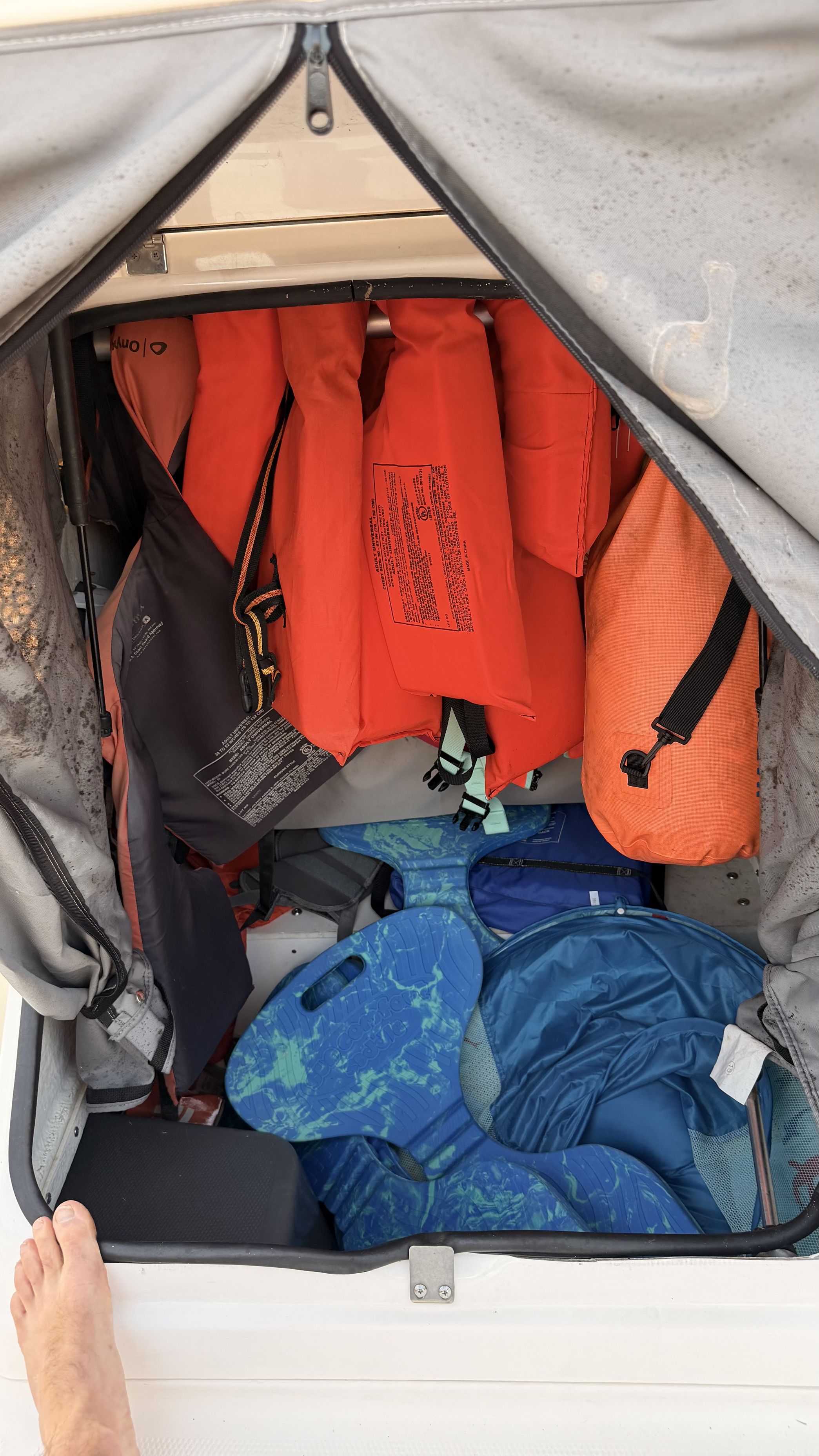 A storage compartment with several orange life jackets and blue flotation devices.