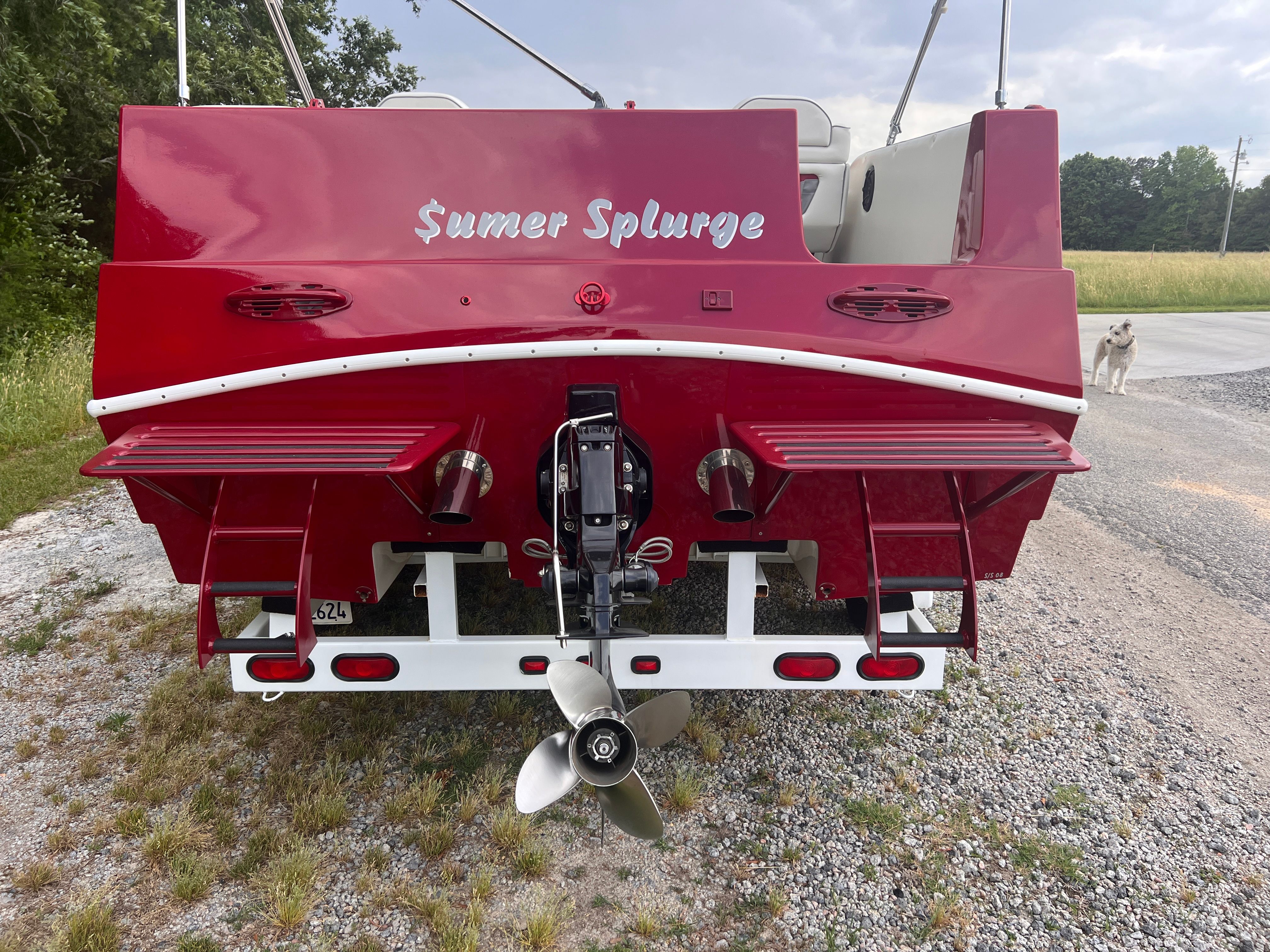 Red boat with two platforms and motor, parked on a gravel path.
