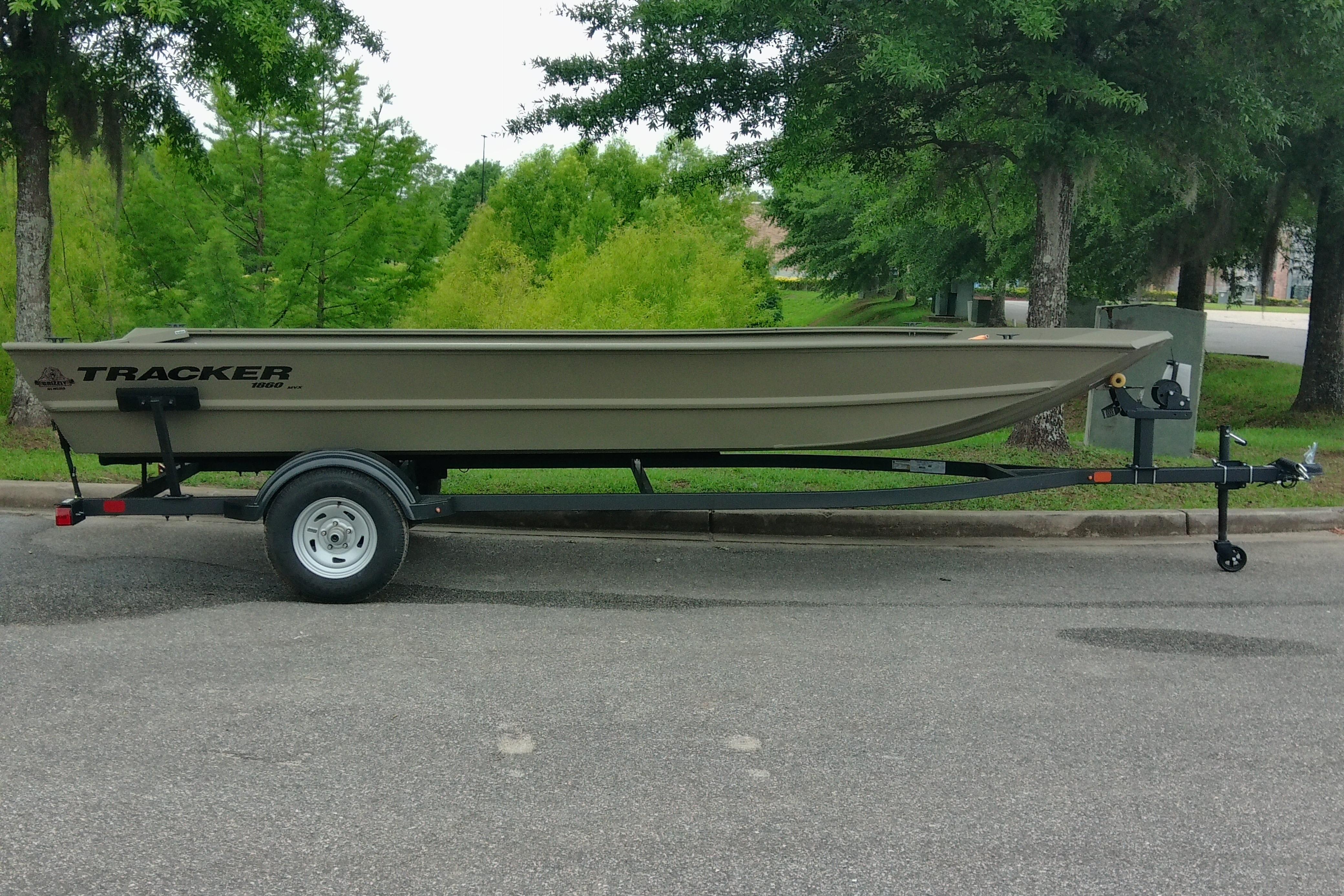 2026 Tracker Grizzly 1860 Utility boat on trailer, parked on a tree-lined street.