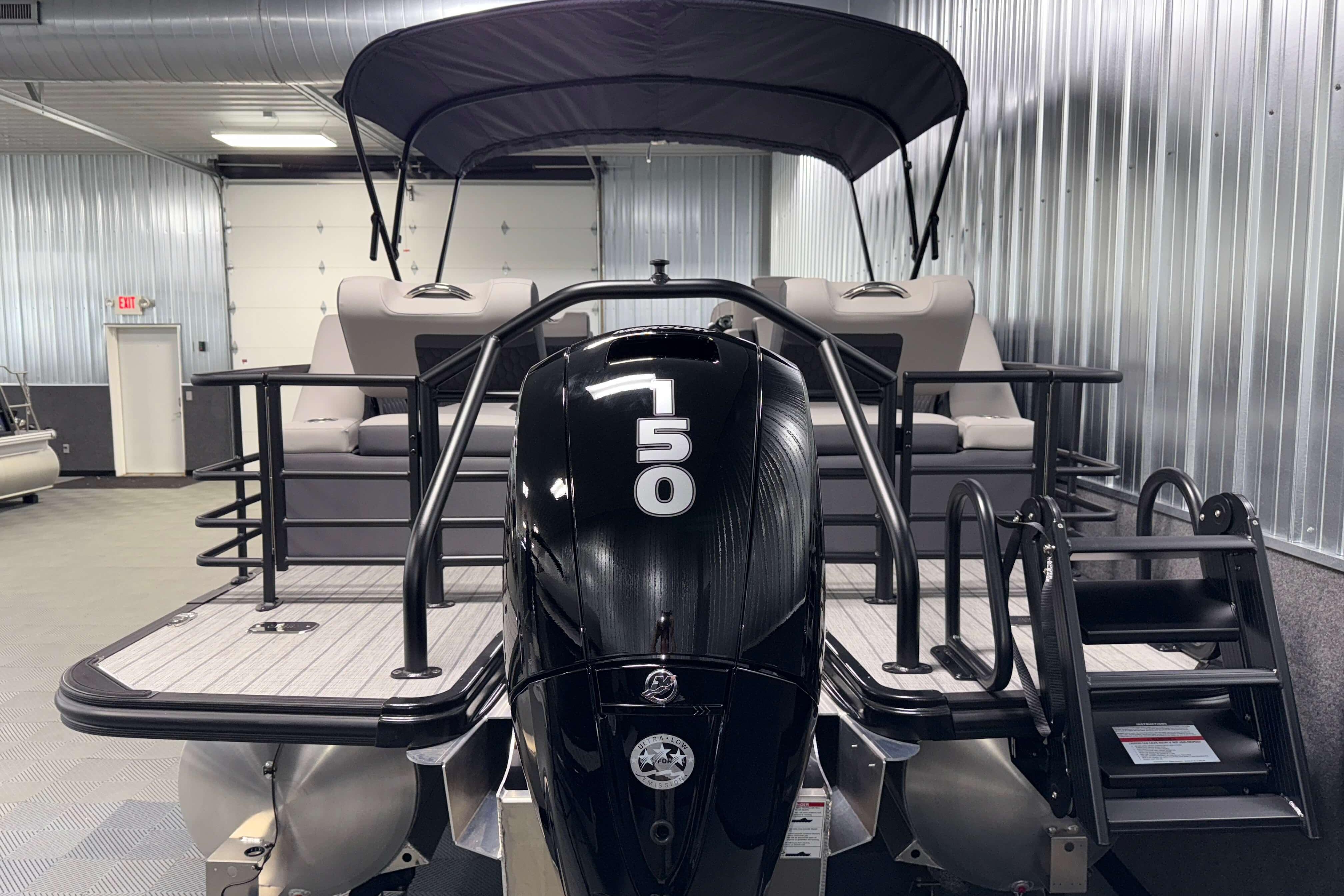 2026 Sylvan L3 SLZ pontoon boat with black motor in a metal-walled showroom.