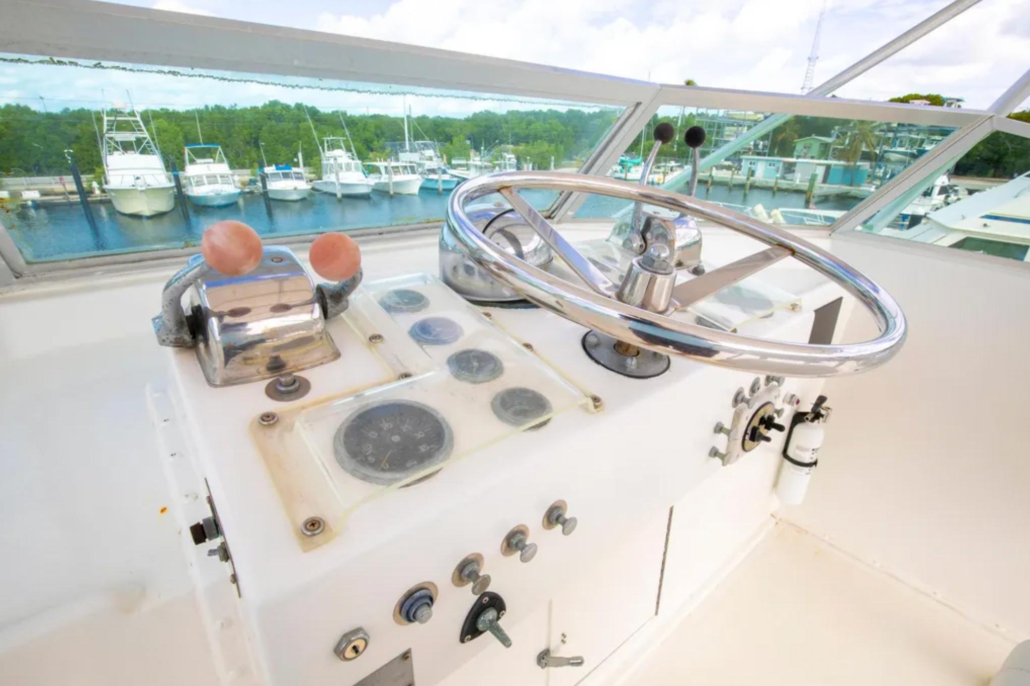 1973 Hatteras 58 Yacht Fisherman helm with steering wheel and controls, docked at marina.