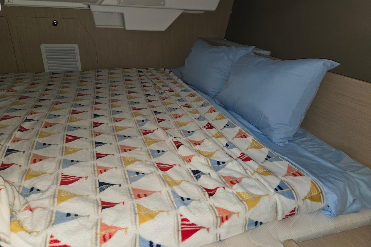 Cozy cabin bed in 2023 Beneteau Oceanis 38.1 yacht with colorful sailboat-patterned blanket.