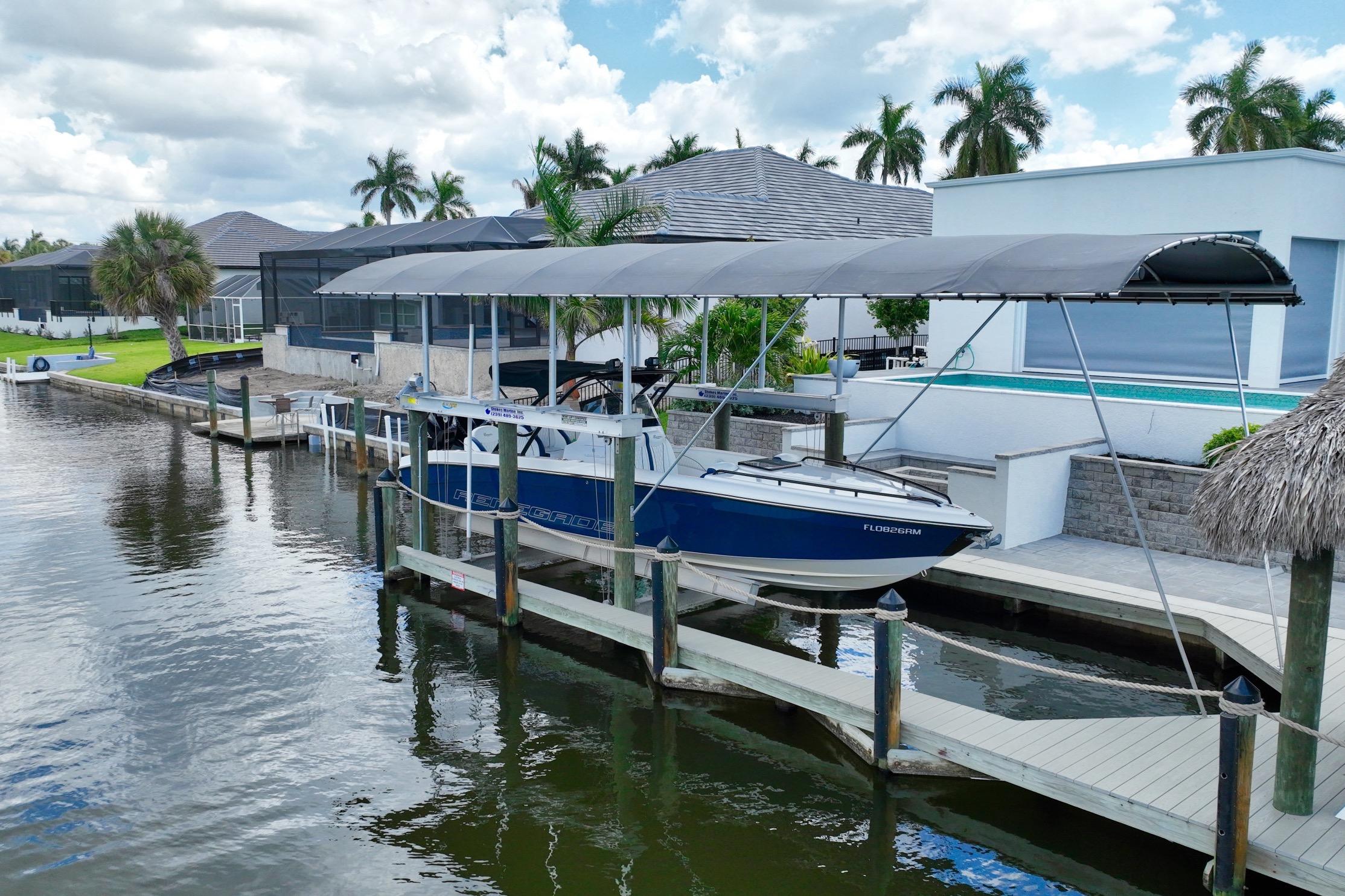 2018 Renegade 32' Cuddy boat docked under canopy, surrounded by waterfront homes and palm trees.