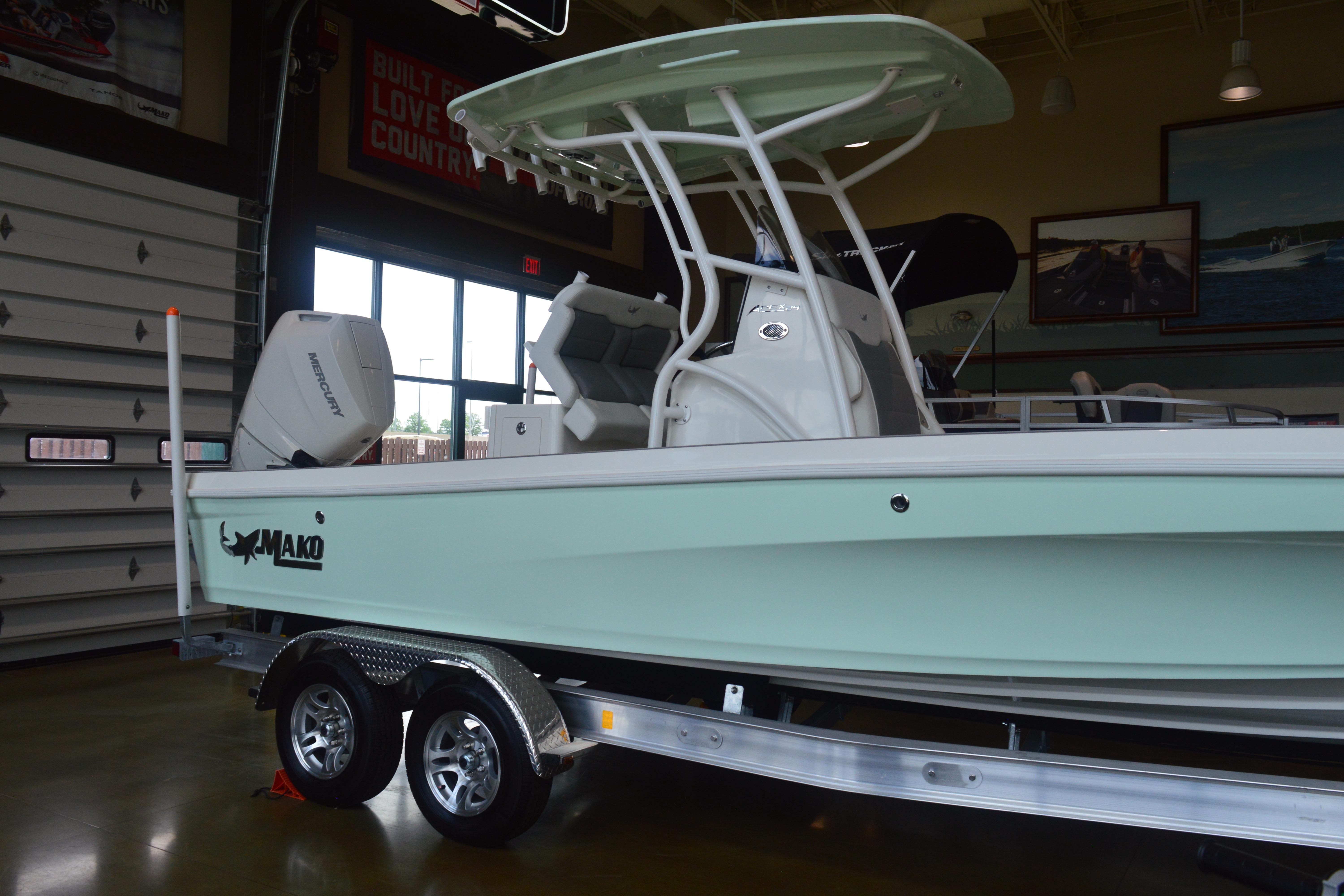2026 Mako 24 APEX boat on trailer in showroom, featuring sleek design and Mercury engine.