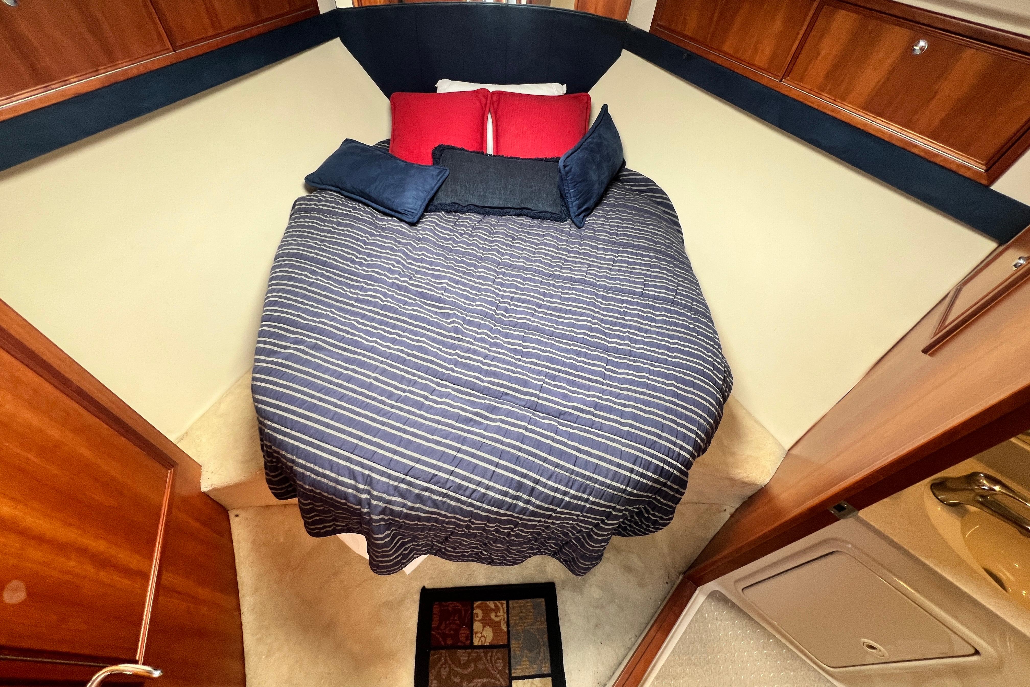 Cozy bedroom in 2007 Riviera 33 Flybridge yacht with striped bedding and wooden cabinetry.