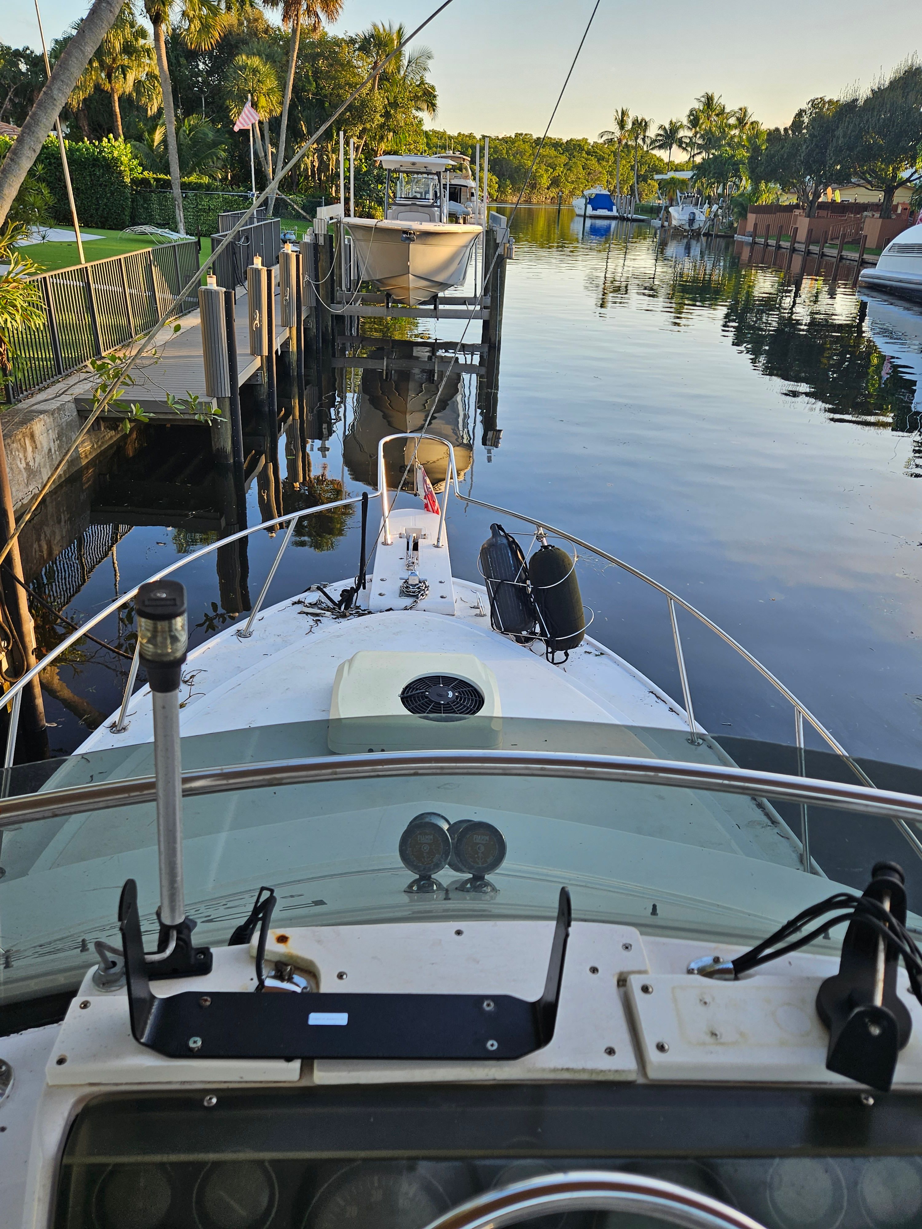 View from a boat's helm overlooking a calm canal lined with palm trees.