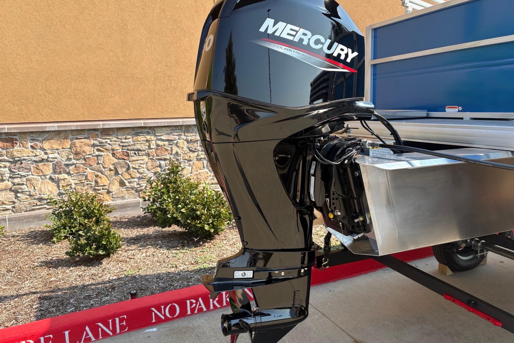 Mercury outboard motor on 2026 Sun Tracker Party Barge 16 DLX, parked near stone wall.