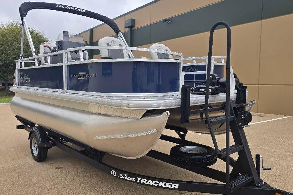 2026 Sun Tracker Bass Buggy 16 XL Select pontoon boat on trailer, parked outdoors.